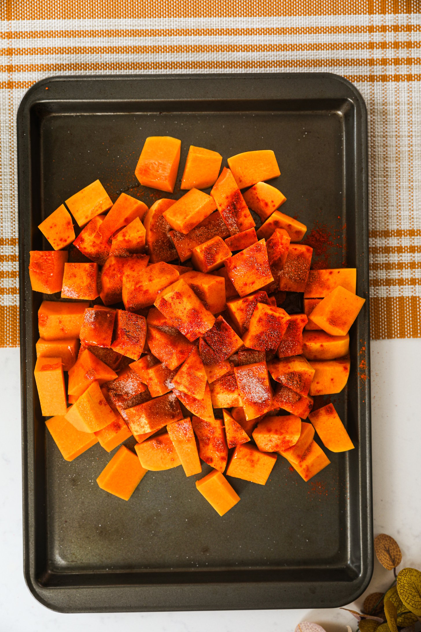 A mound of butternut chunks generously dusted with powdered spices, arranged on an oven tray.