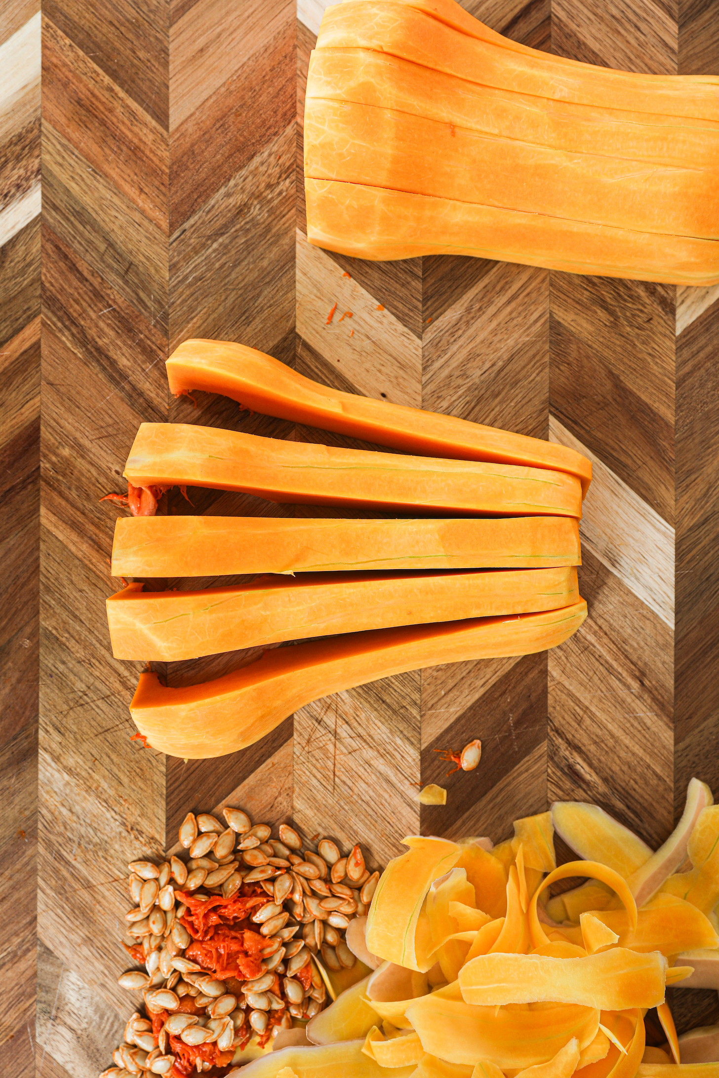 Two halves of butternut squash, each sliced into five pieces, with seeds and peelings on the side.