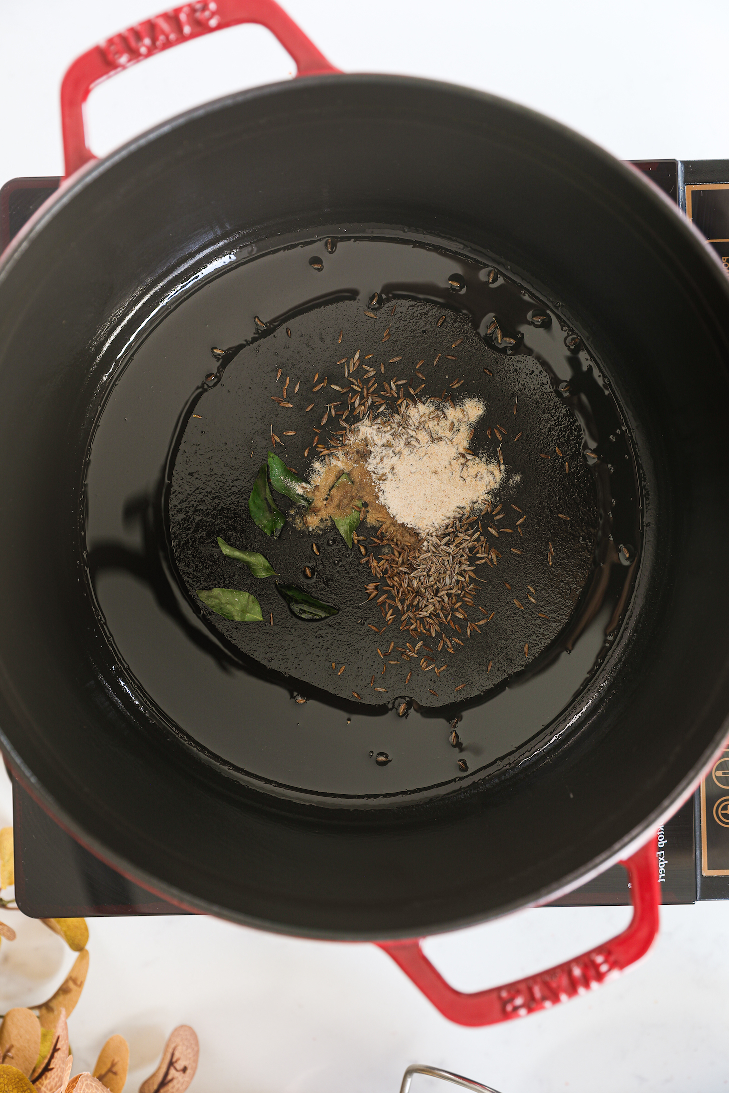 A cast iron pot with oil, cumin seeds, curry leaves and a white powder.