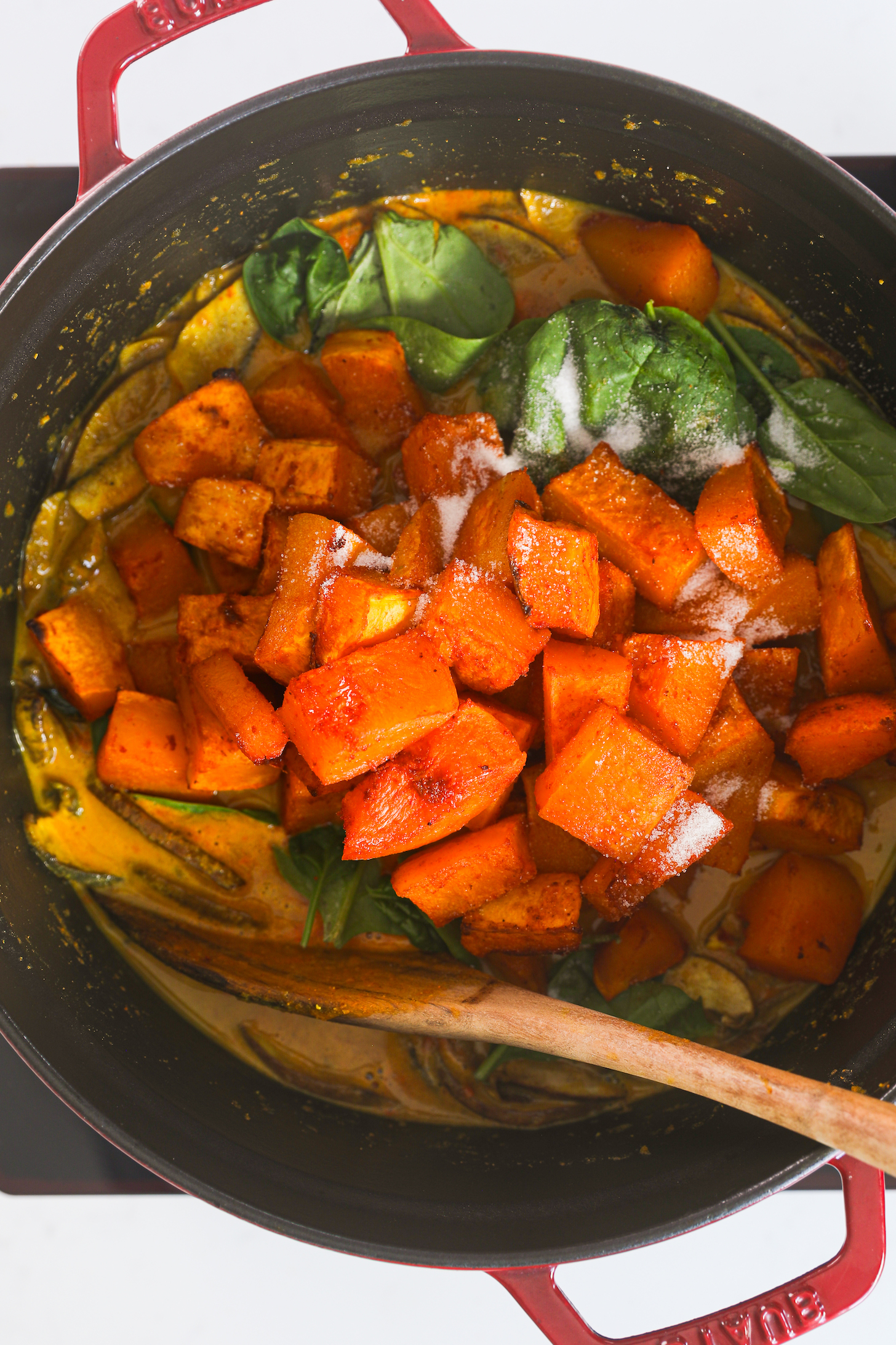 A cooking pot featuring a mound of roasted butternut squash, delicately layered on a bed of fresh spinach and sauce.