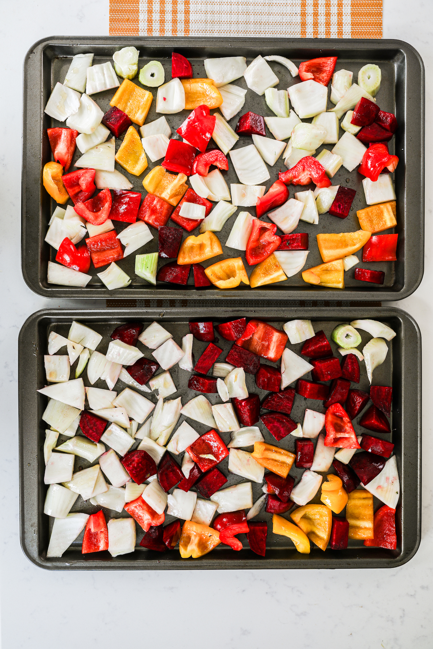 Two baking trays holding an assortment of mixed vegetables, including neatly arranged cubed beets, peppers, and fennel.
