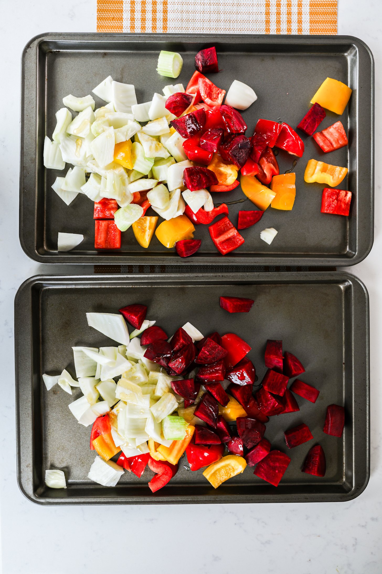 Two baking trays showcasing a medley of mixed vegetables, featuring cubed beets, diced peppers, and chopped fennel.