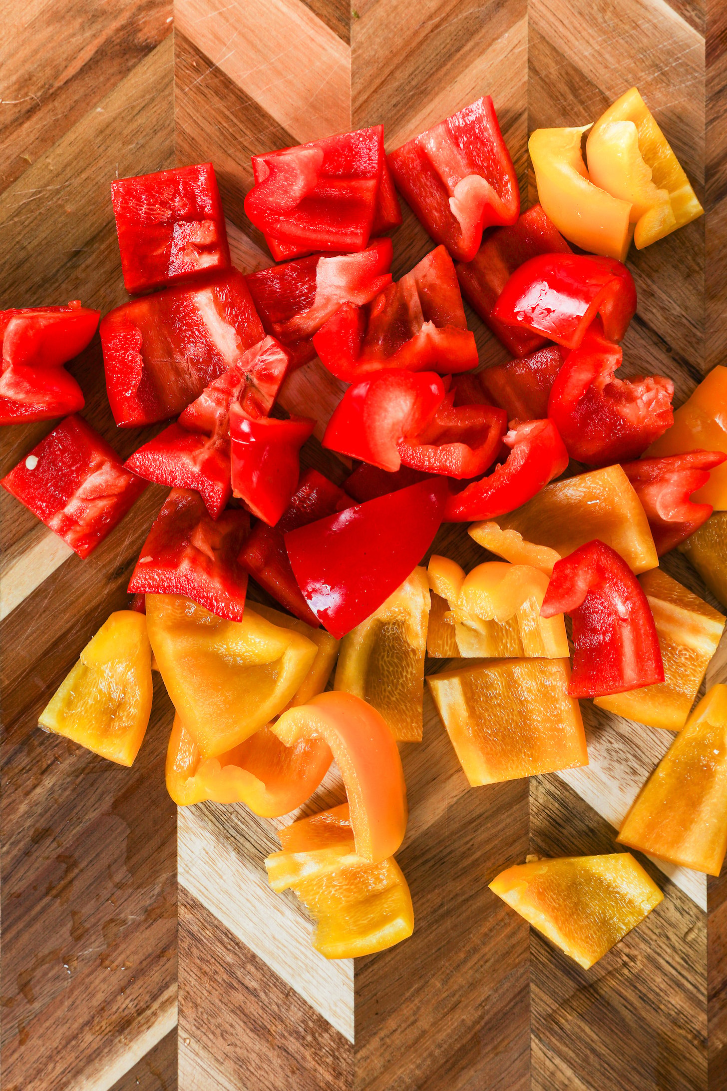 A collection of medium-sized, chopped yellow and red peppers placed on a chopping board.