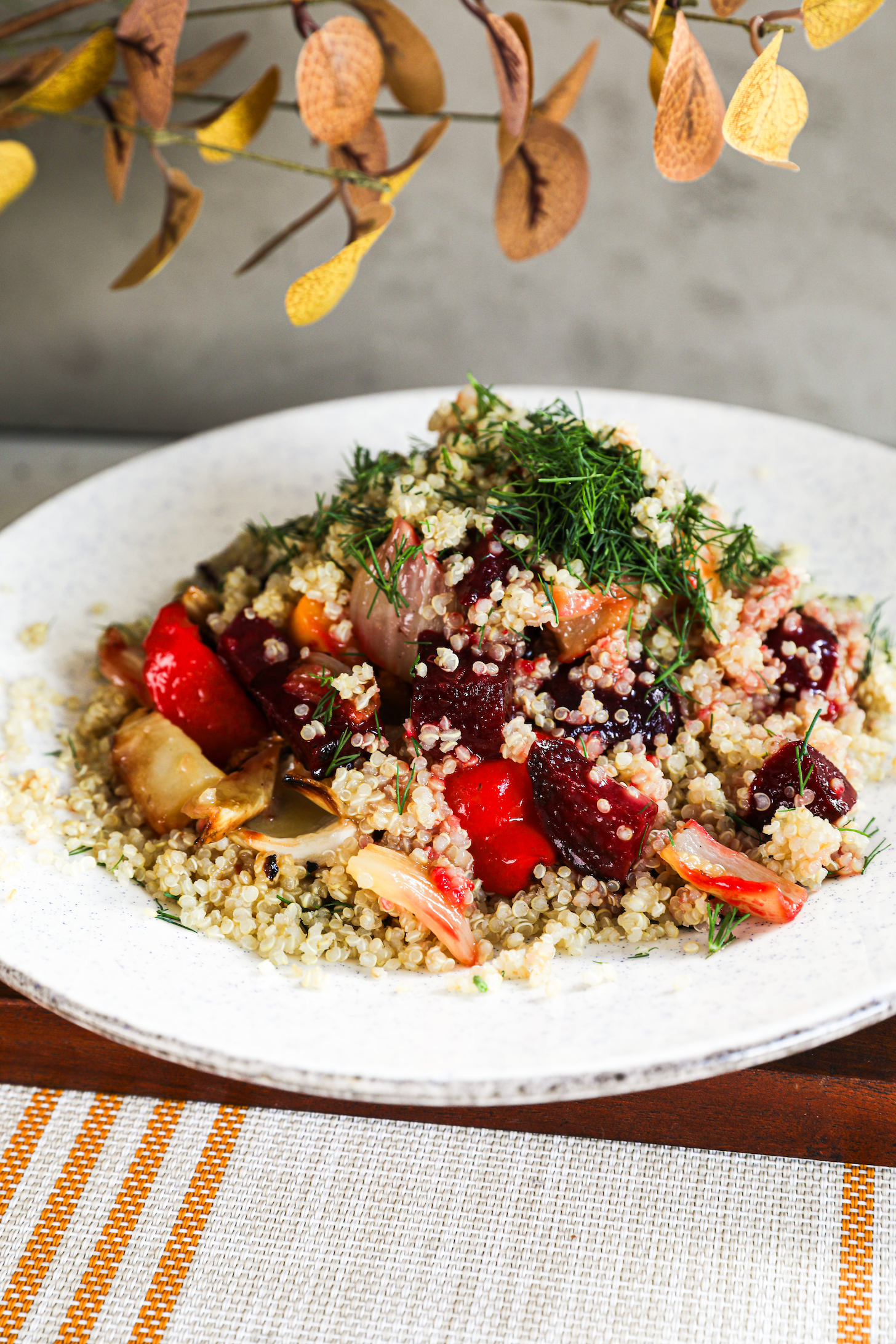 A plate of salad featuring a delightful mixture of quinoa, roasted beets, peppers, and fennel, topped with dill and doused in dressing.