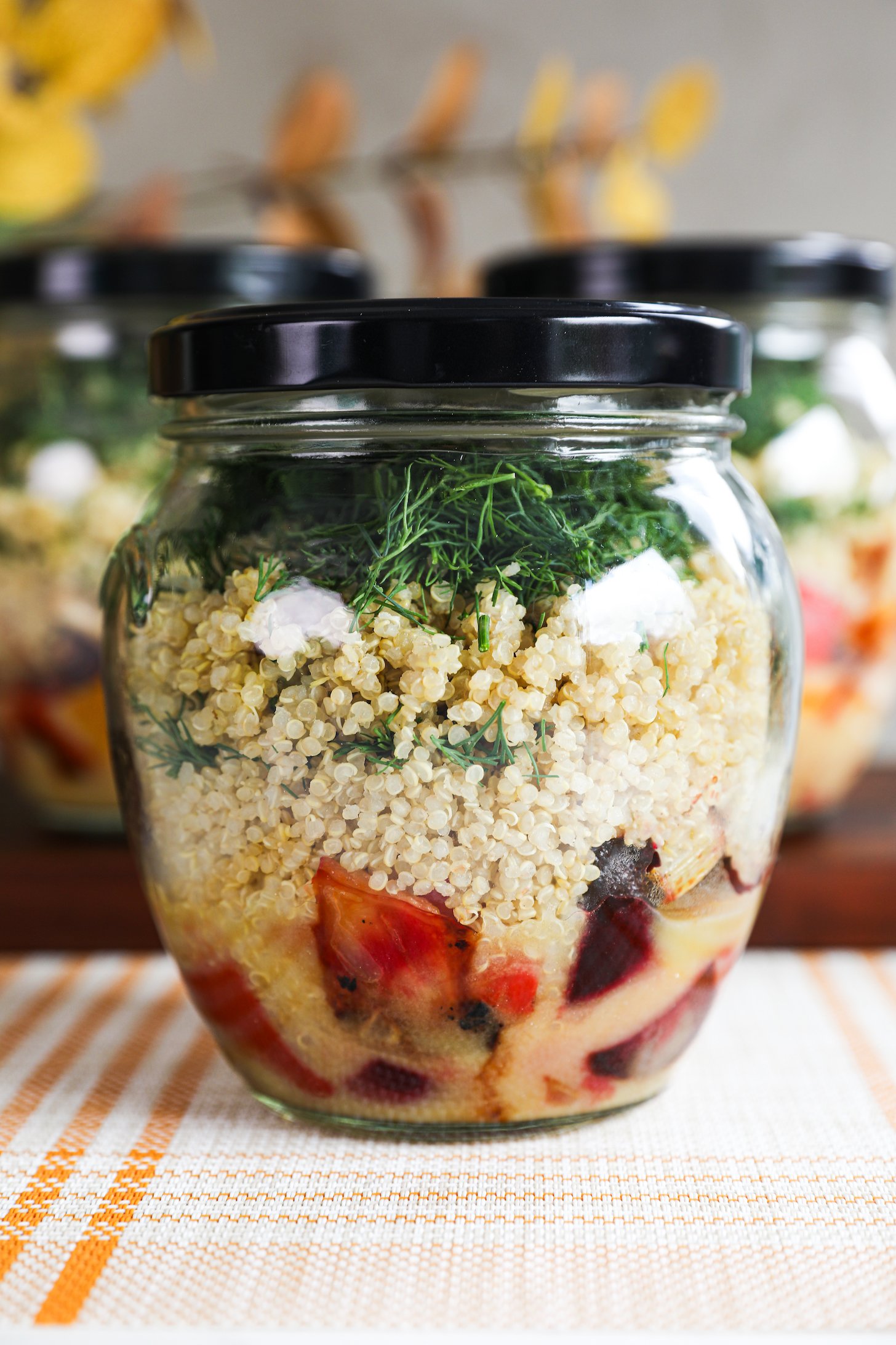 A close up of a glass jar of salad layered with dressing, veggies, quinoa and dill.