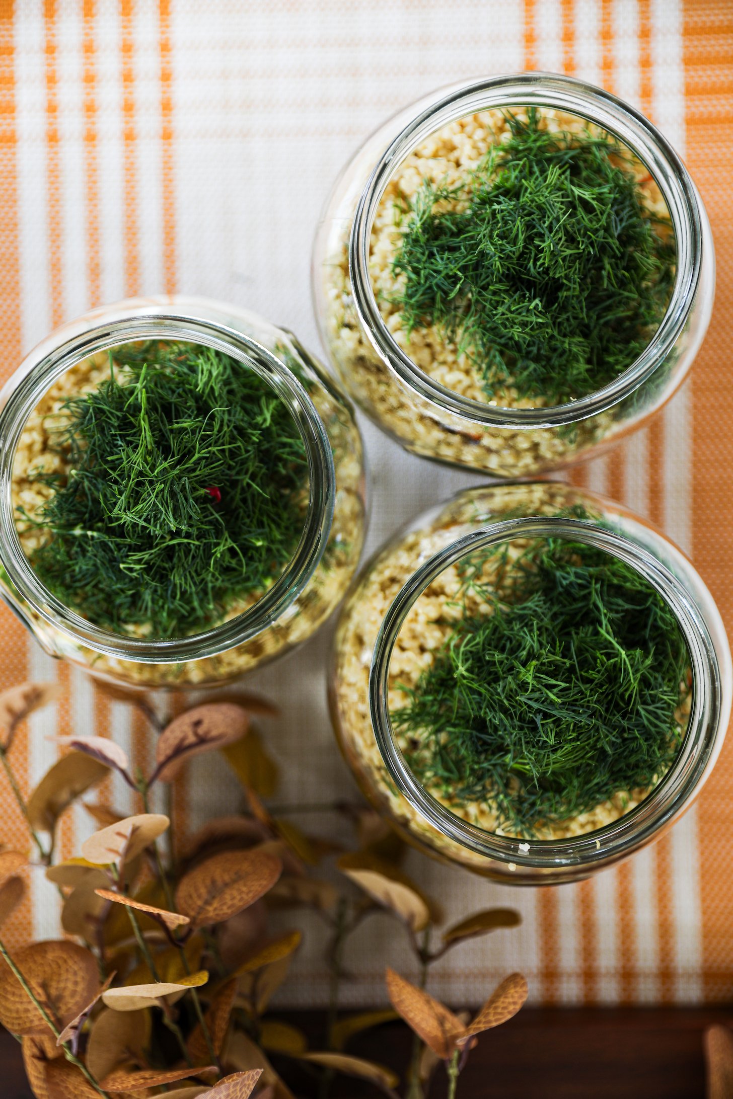 Three glass jars with quinoa topped with chopped fresh dill.