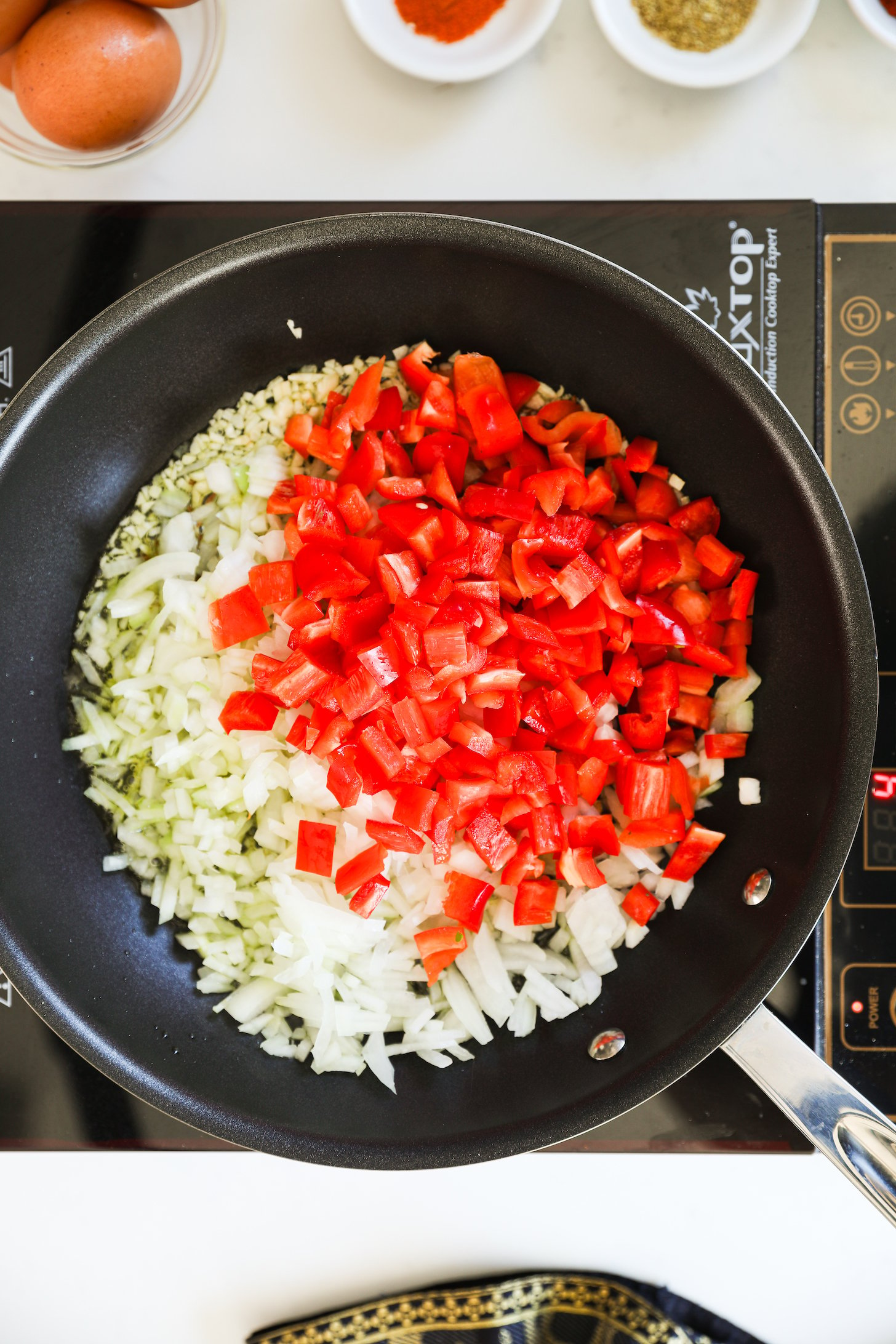 An image of a cooking pan with freshly chopped red peppers and onions placed on a mobile stovetop.