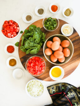 A selection of food ingredients including eggs, spinach, chopped vegetables and ramekins of spices on a lazy Susan.