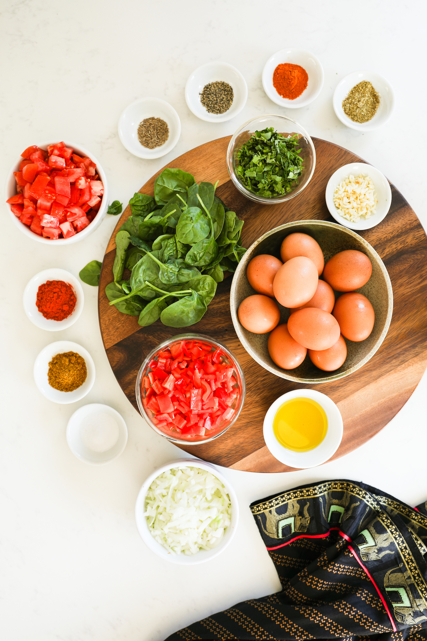 A selection of food ingredients including eggs, spinach, chopped vegetables and ramekins of spices on a lazy Susan.