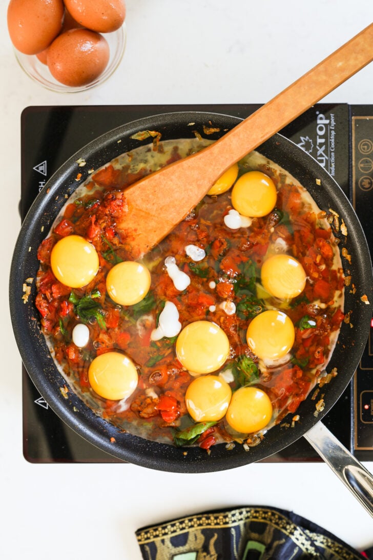 A pan with a tomato base topped with 10 raw eggs on a mobile cook top.
