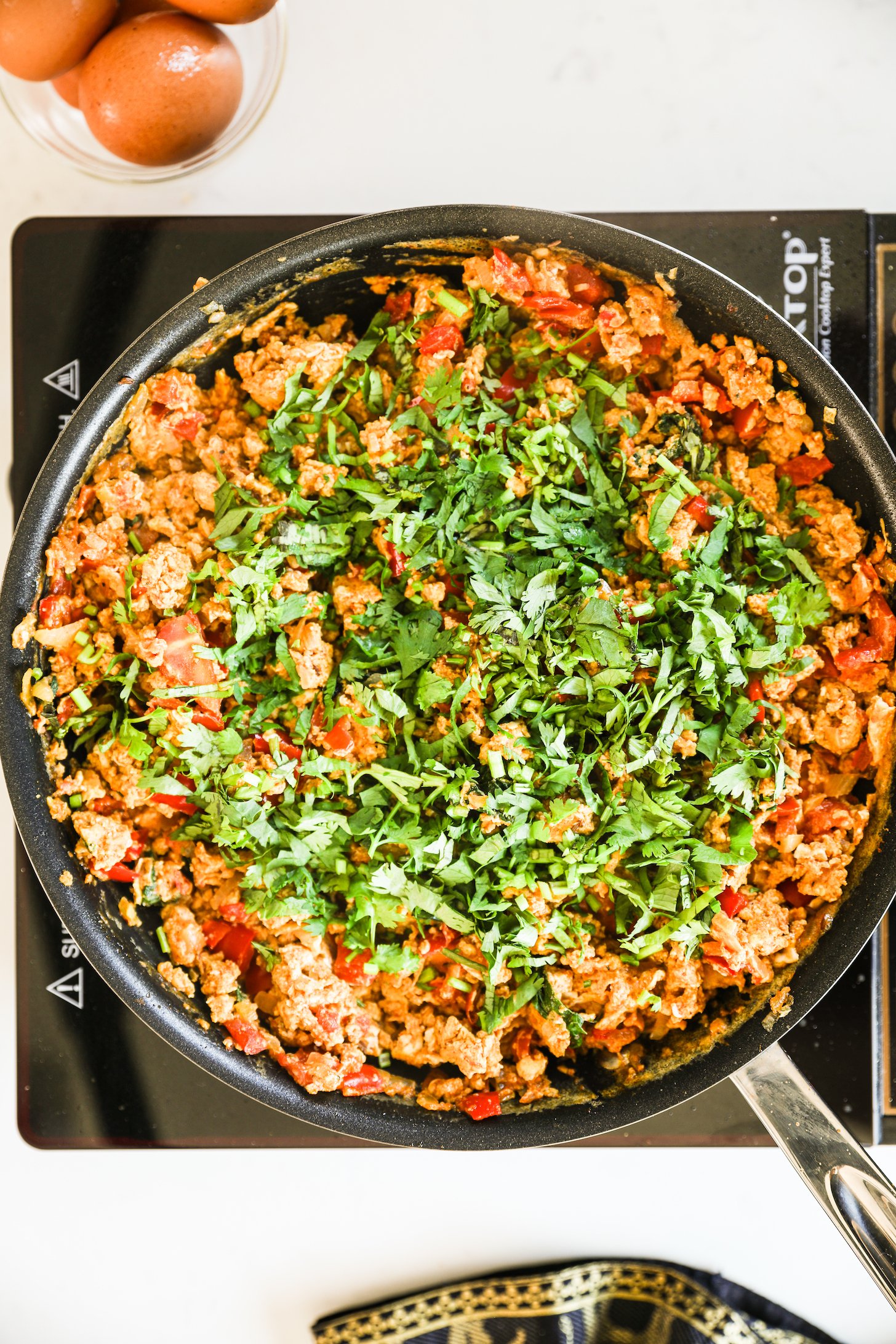 Image of a pan on a portable stove containing scrambled eggs with vegetables inside, garnished with chopped cilantro.
