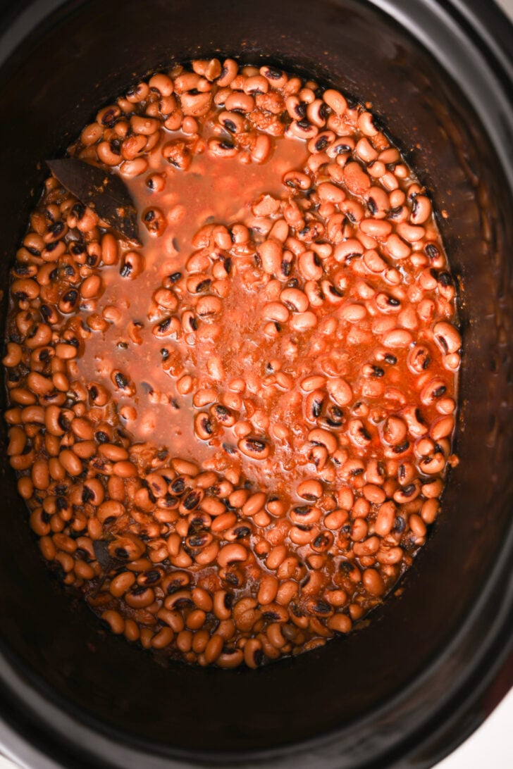 Flatlay image featuring a slow cooker filled with black-eyed peas submerged in a vibrant red sauce.