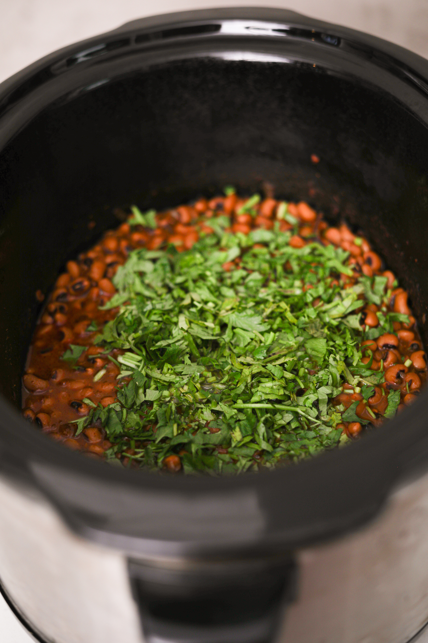 Image of a slow cooker filled with black-eyed peas in a tomato sauce, garnished with finely chopped cilantro.