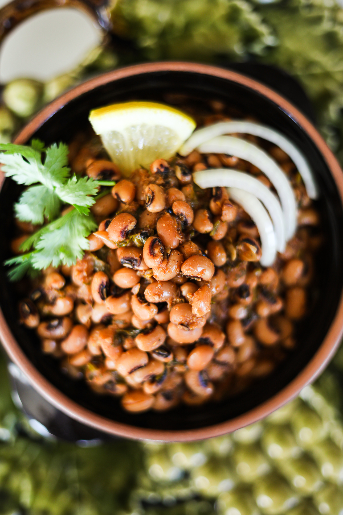 Close up image of a clay pot with lobia curry or black eyed peas garnished with lemon slice, onion and cilantro.