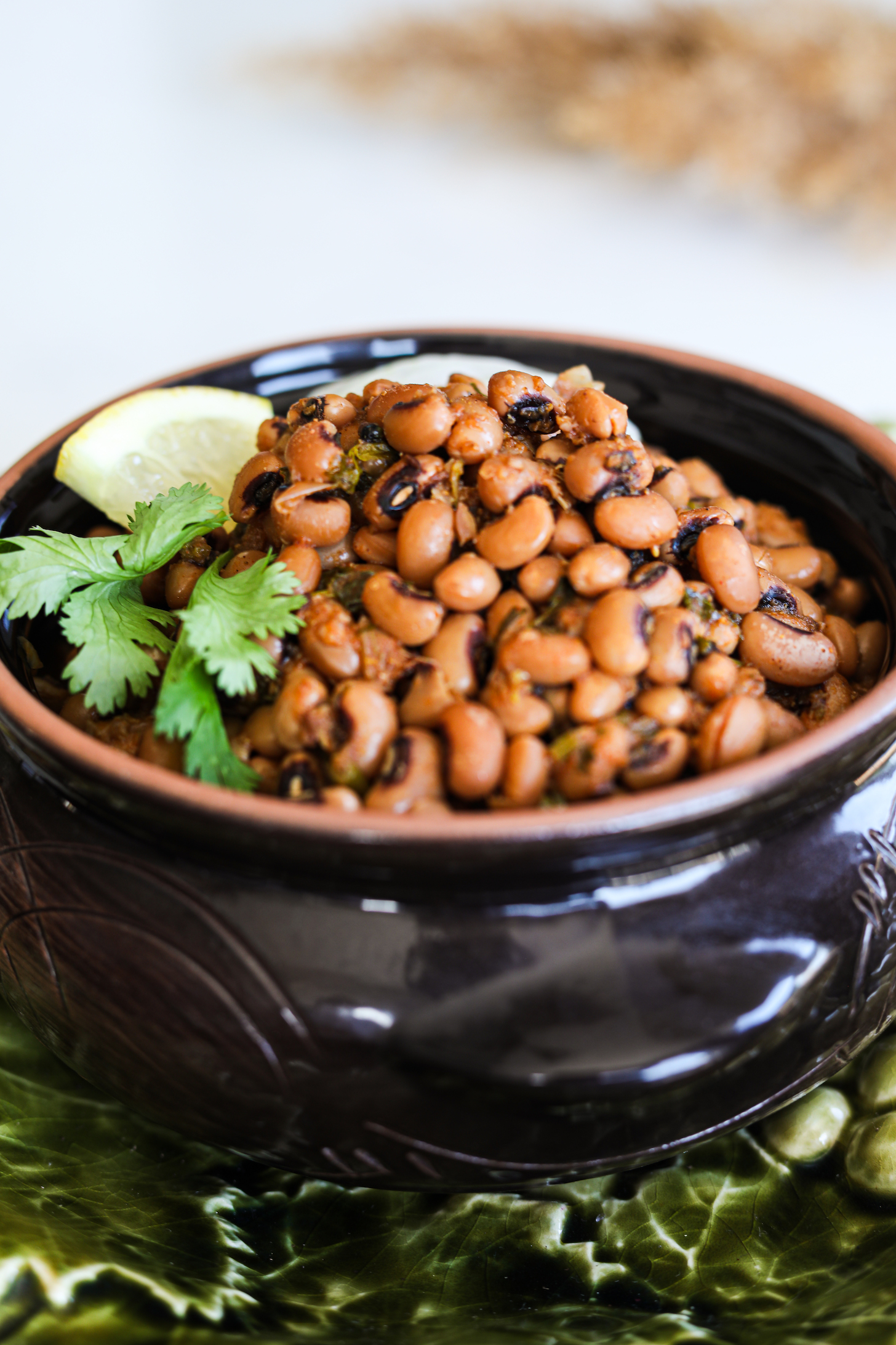 A perspective image of black eyed peas, aka lobia curry served in a clay pot topped with lemon segments and cilantro.