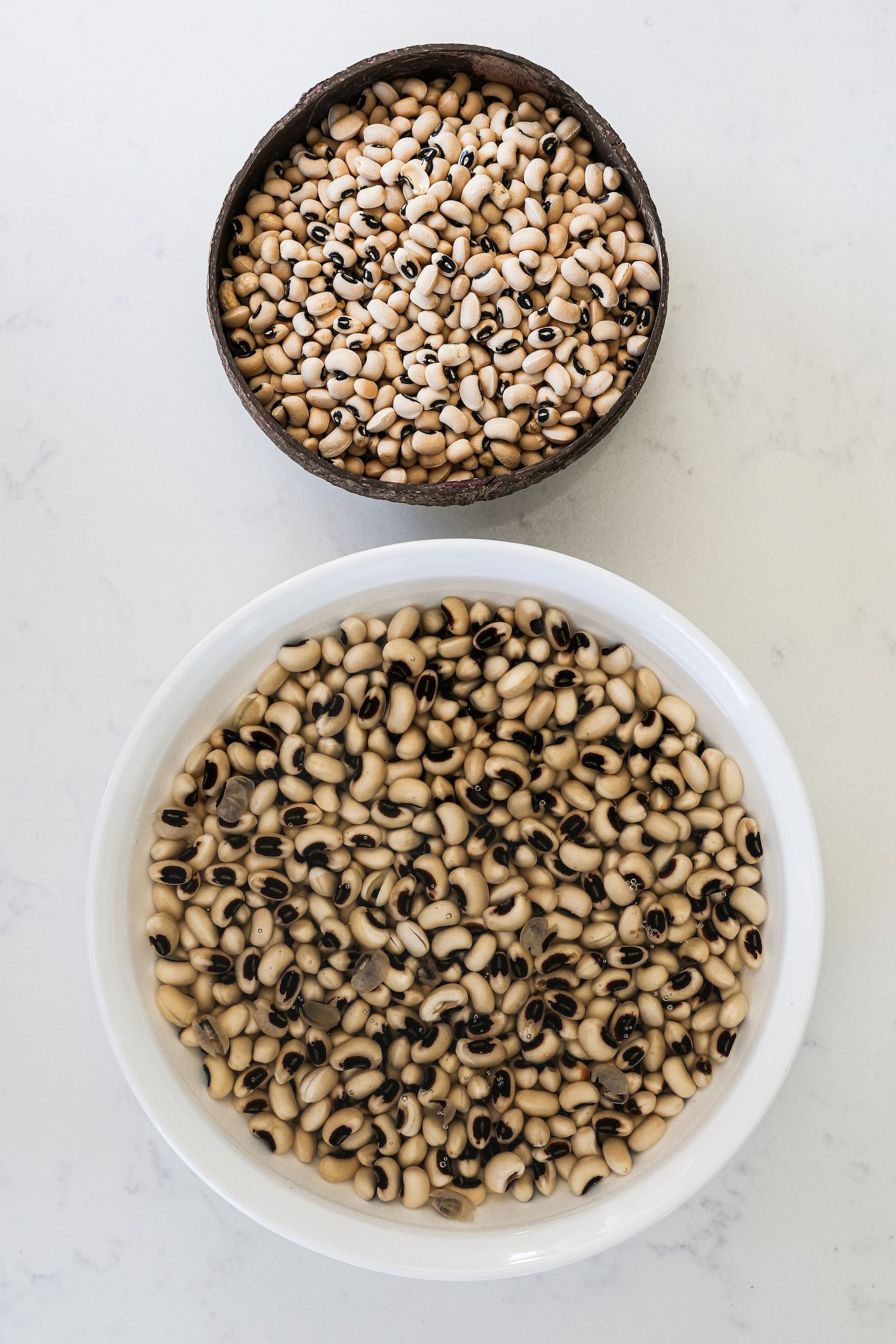 Two bowls: one containing dry black-eyed peas, and the other with black-eyed peas submerged in water.