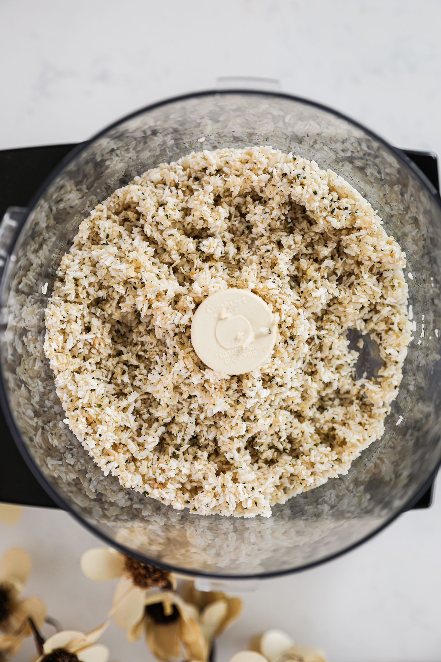 An overhead view of a food processor with a mixture of coconut and hemp seeds.