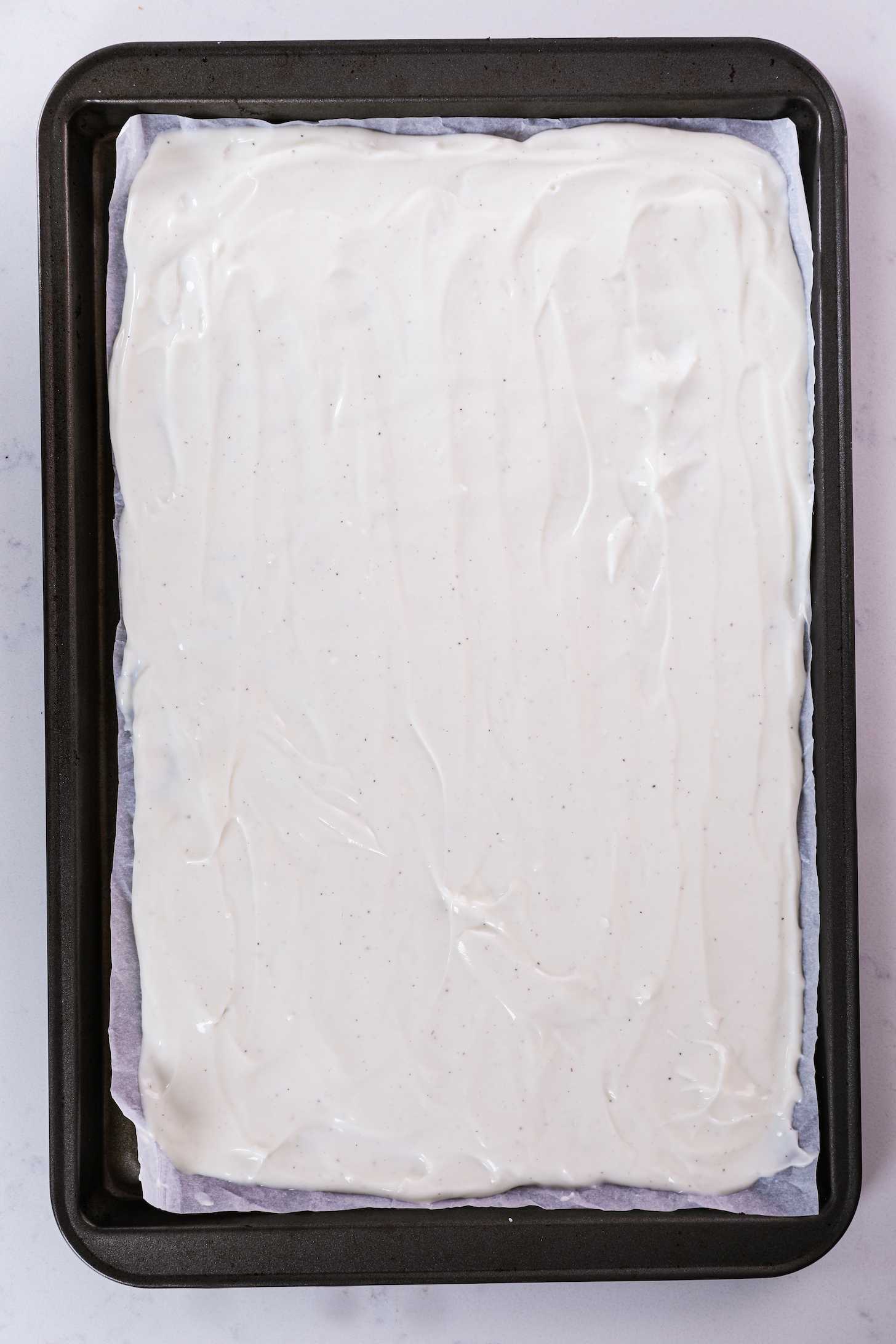 A smooth layer of frozen yogurt on a tray with raised edges and parchment paper lining.