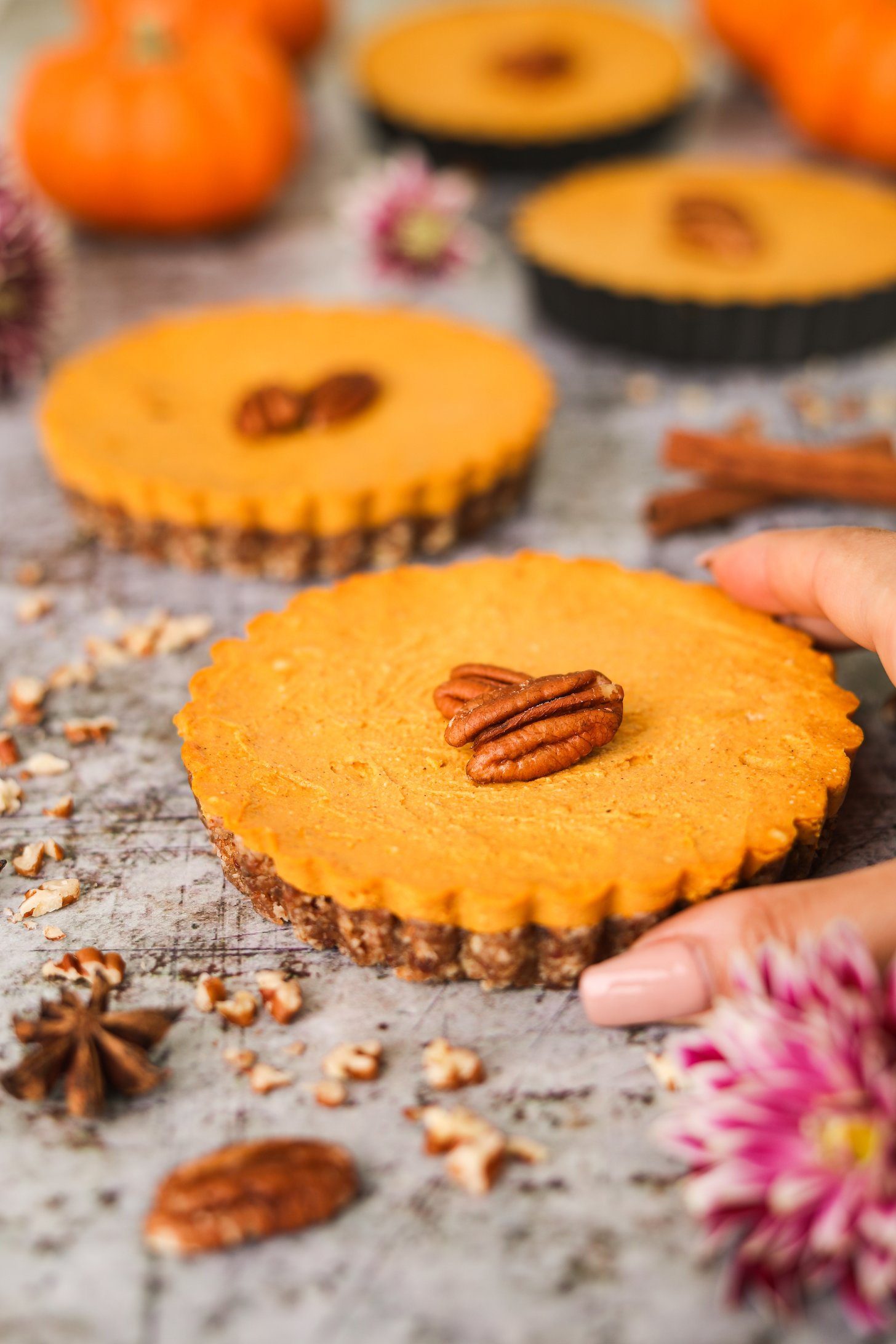 Perspective image of four mini pumpkin pies, with a hand reaching towards the one in the front.