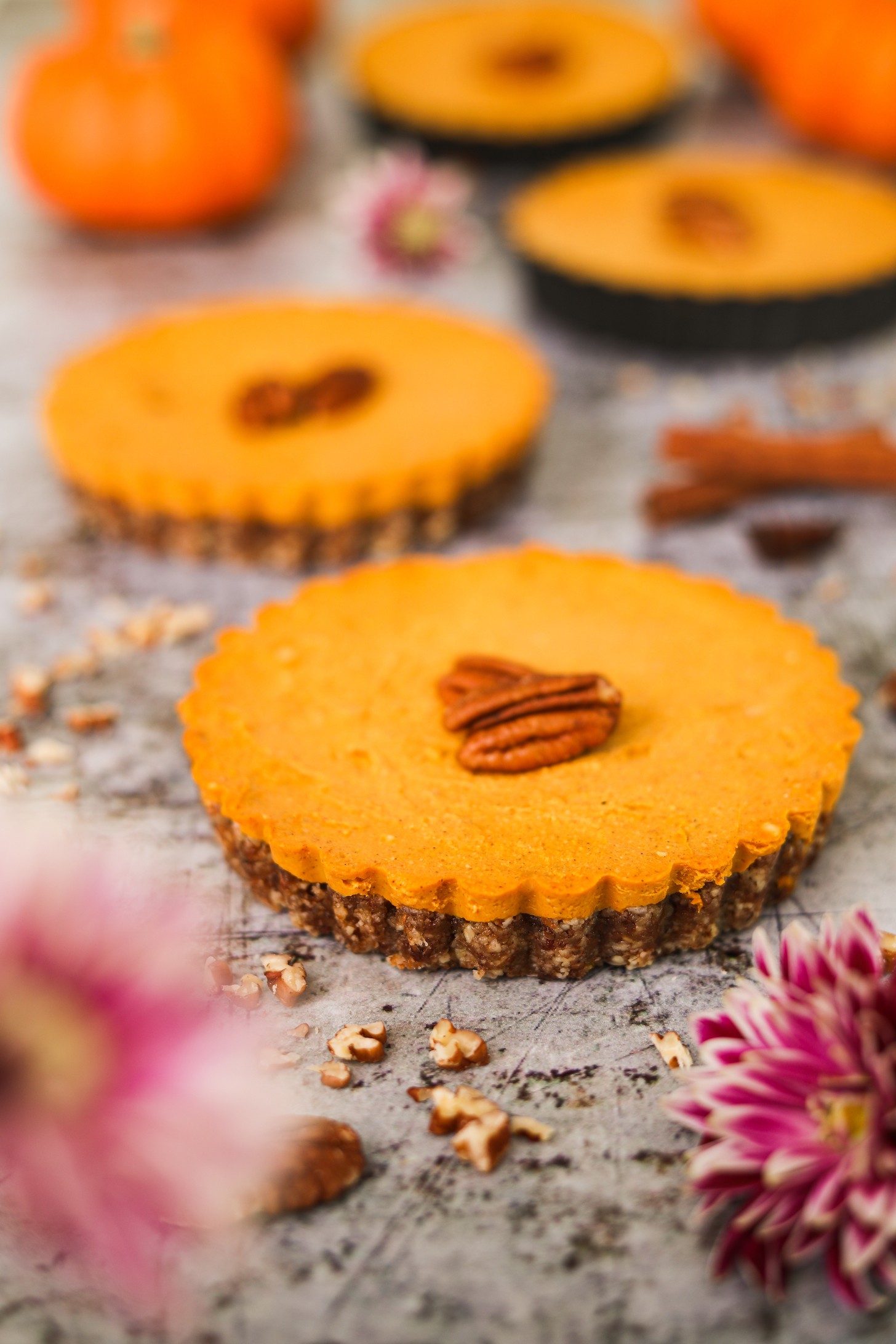 Perspective image of four mini pumpkin pies decorated around flowers, nuts and spices.