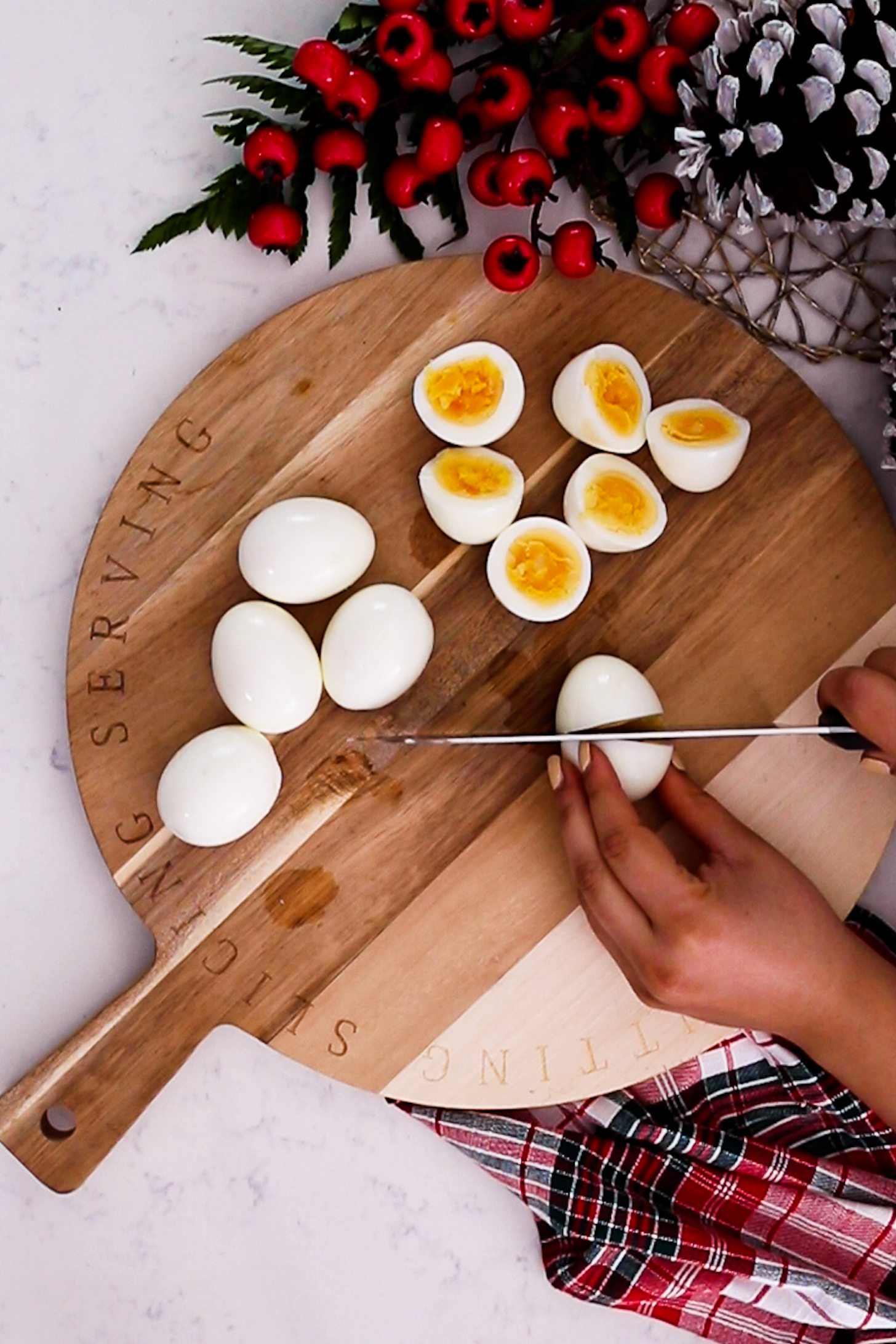A hand is seen slicing a boiled egg in half with a knife, surrounded by a collection of more boiled eggs.