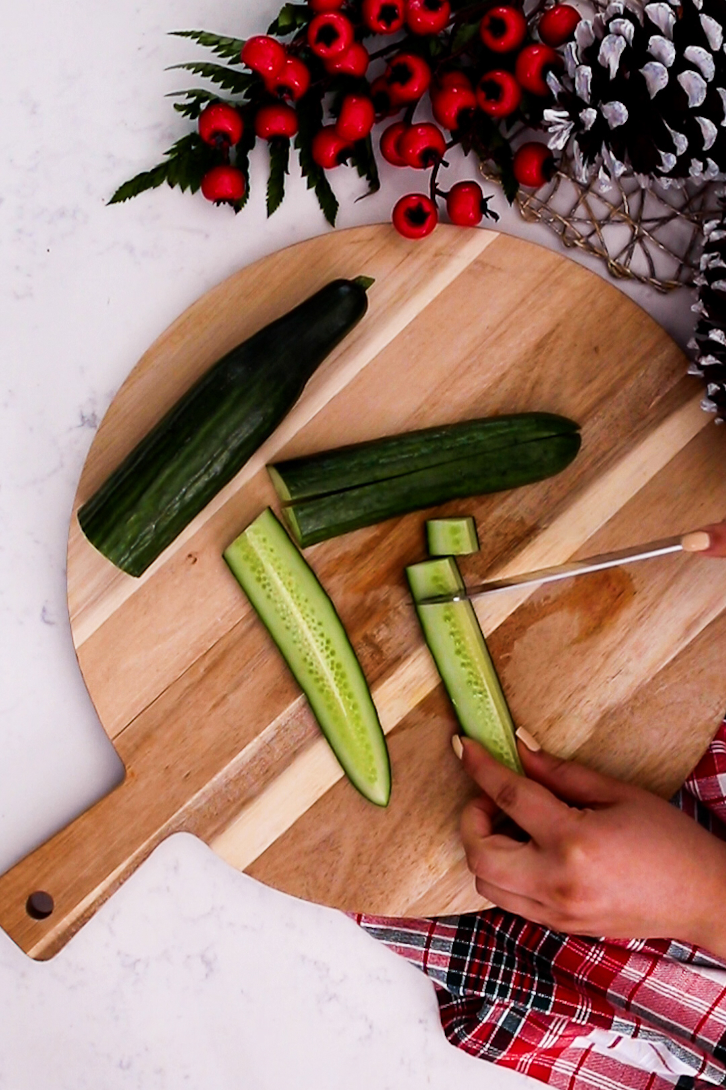 A hand is seen slicing a cucumber with a knife, surrounded by festive decorations.