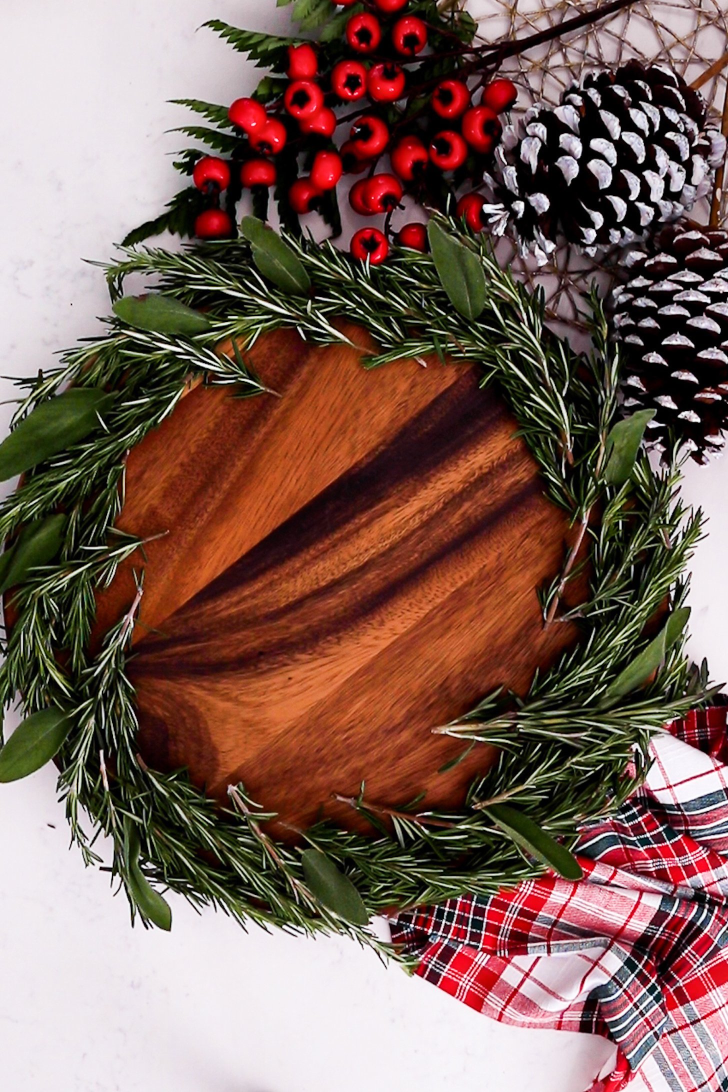 On a lazy Susan, a thick layer of fresh rosemary and few sage leaves line the edge, surrounded by festive decorations