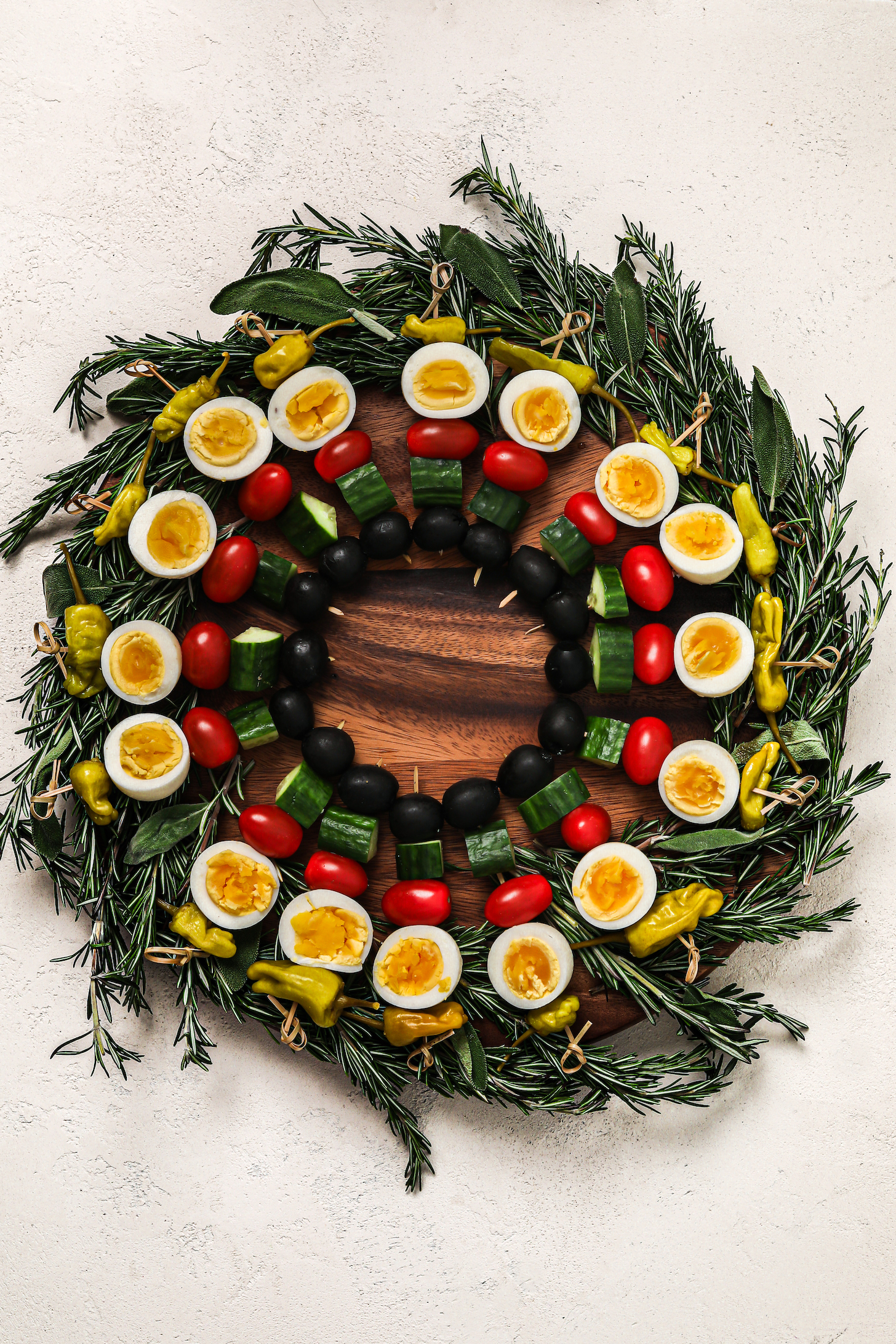 Colourful and festive wreath of wooden picks threaded with boil egg halves, veggies and chilli peppers on a bed of rosemary and sage.