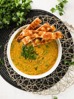 Naan strips delicately placed atop a large bowl of creamy soup garnished with fresh parsley leaves.