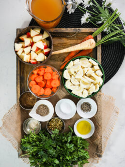 Stylishly arranged diced parsnips, carrots, apples, spices, parsley, and stock seen from above.