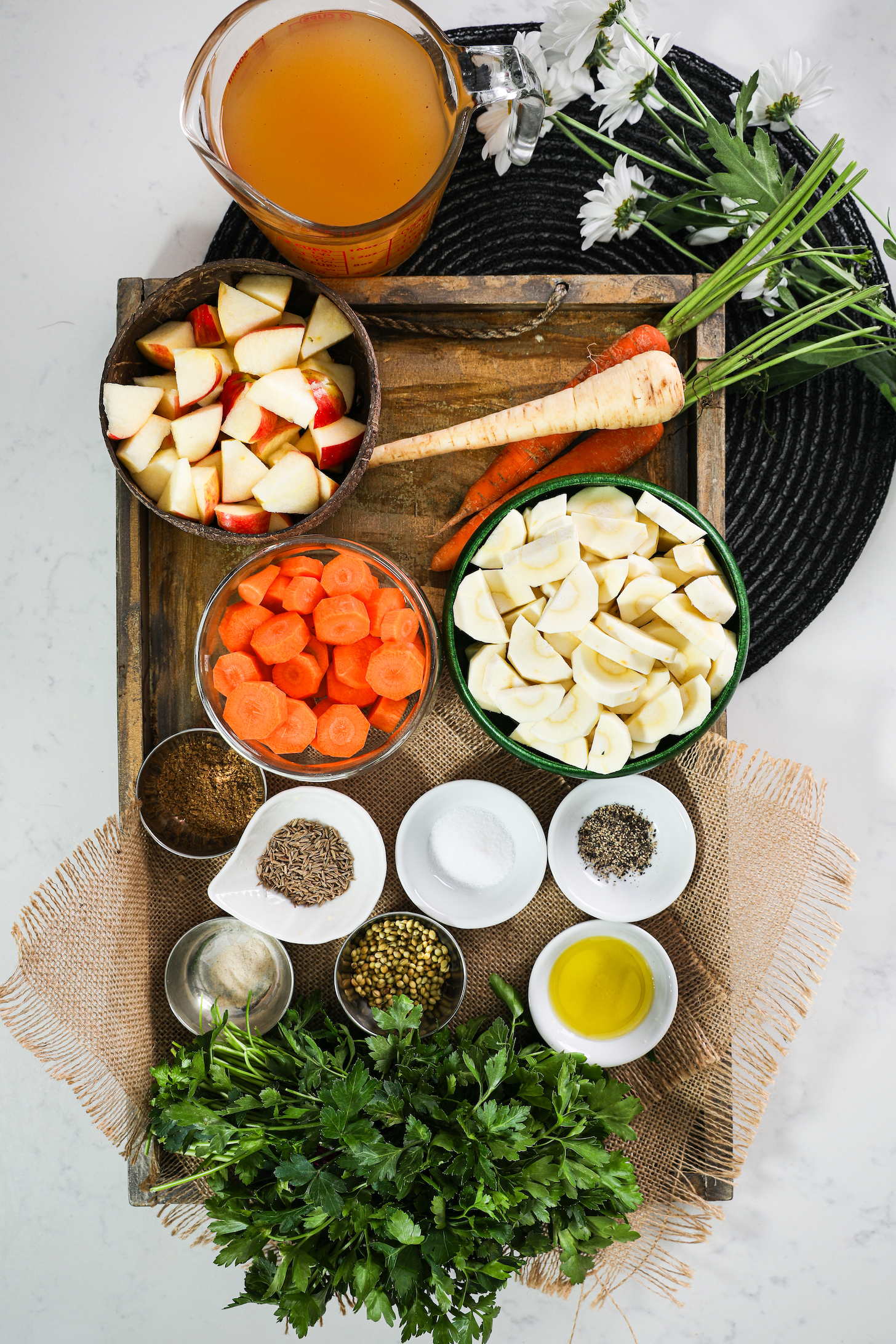 Stylishly arranged diced parsnips, carrots, apples, spices, parsley, and stock seen from above.