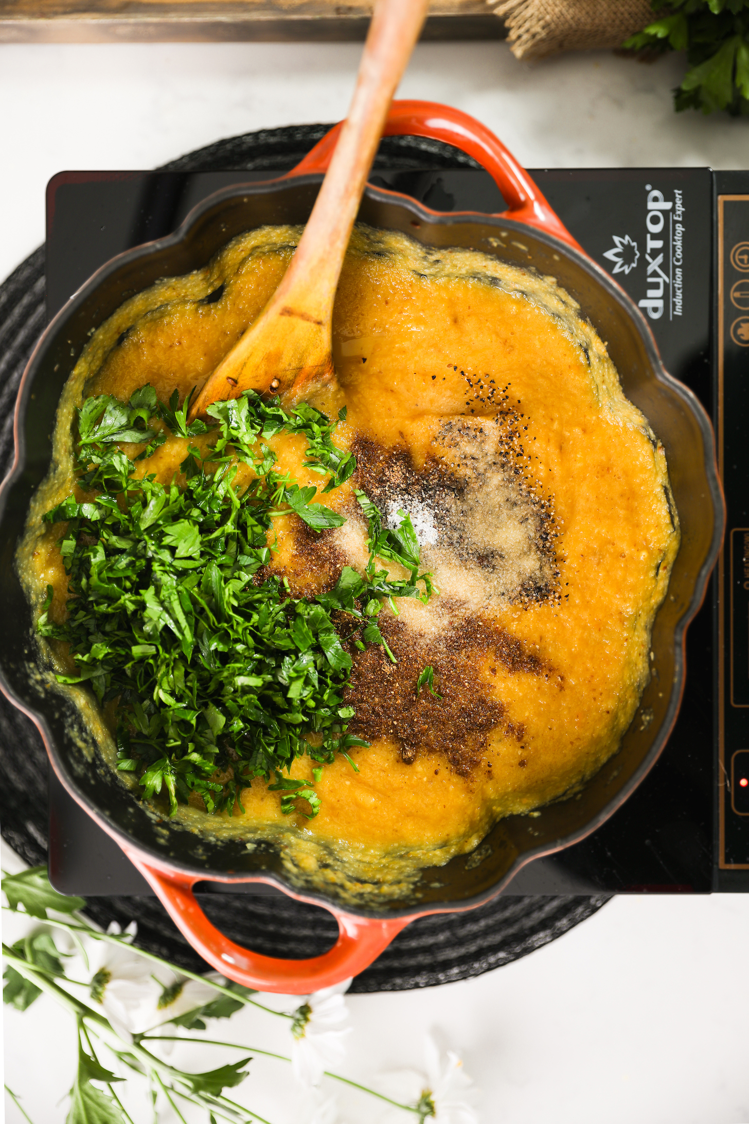 تصویر بالای یک دیگ آشپزی با سوپ خامه ای که روی آن جعفری خرد شده، گارام ماسالا و نمک است.