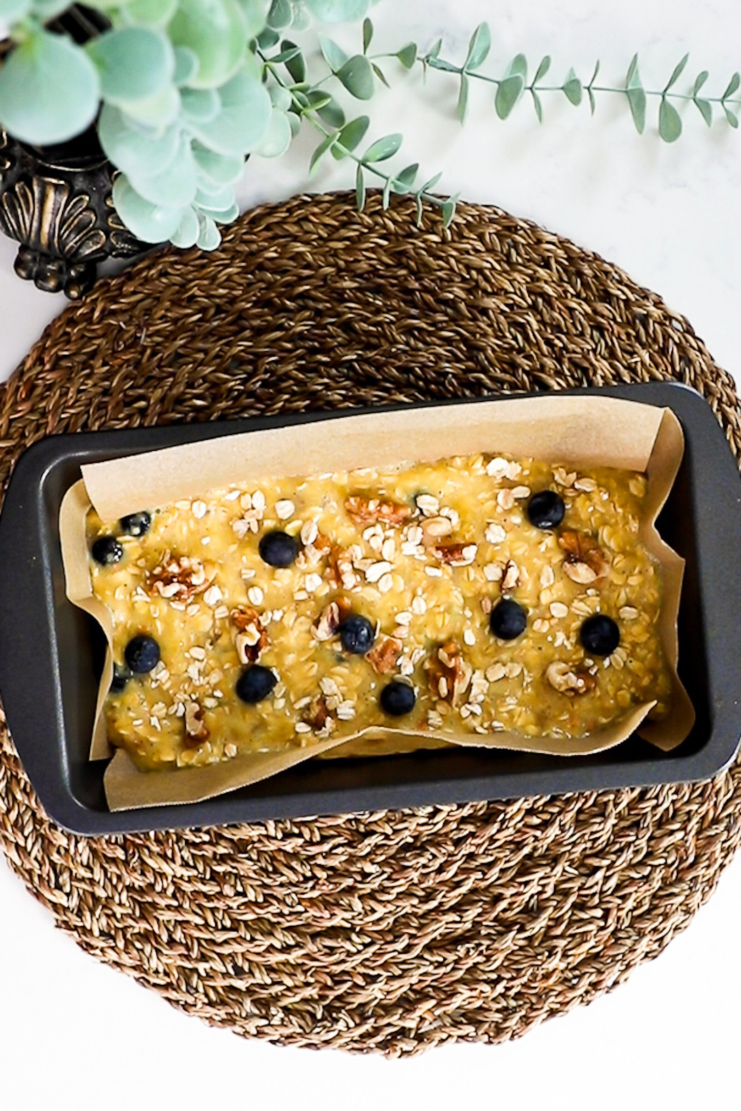 Loaf pan filled with wet oat mixture topped with blueberries and walnuts.