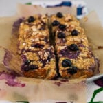 Plate of six sliced baked oatmeal squares topped with blueberries and walnuts.