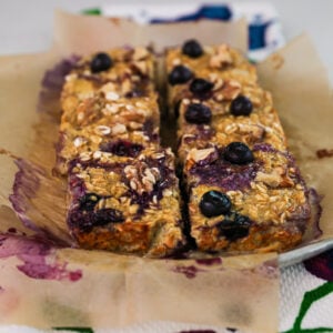 Plate of six sliced baked oatmeal squares topped with blueberries and walnuts.