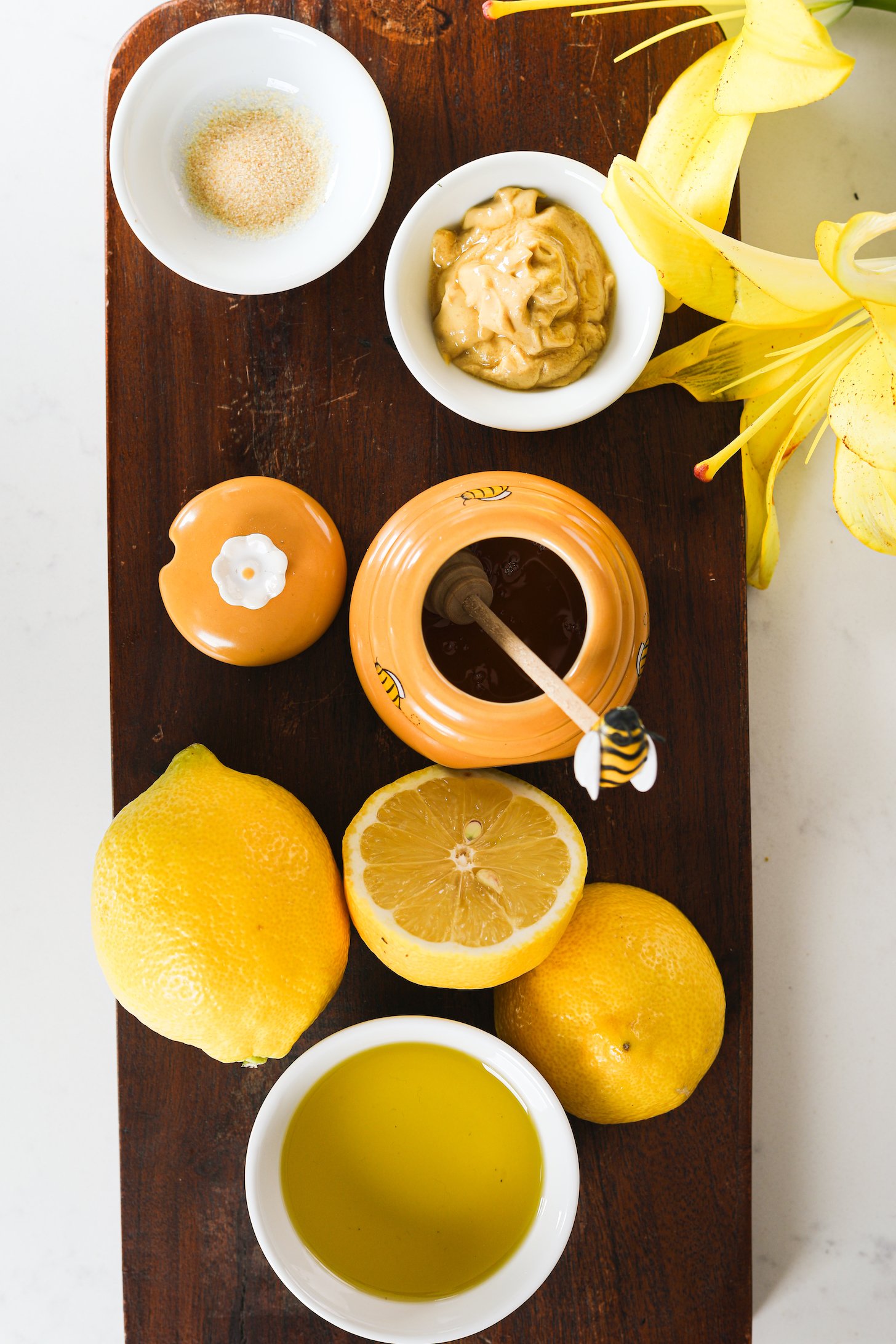 A display of food ingredients showing lemon, honey, mustard, oil and garlic on a dark wooden board.