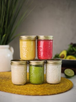 Five colourful salad dressings arranged in mason jars; three jars at the base and two jars stacked on top.