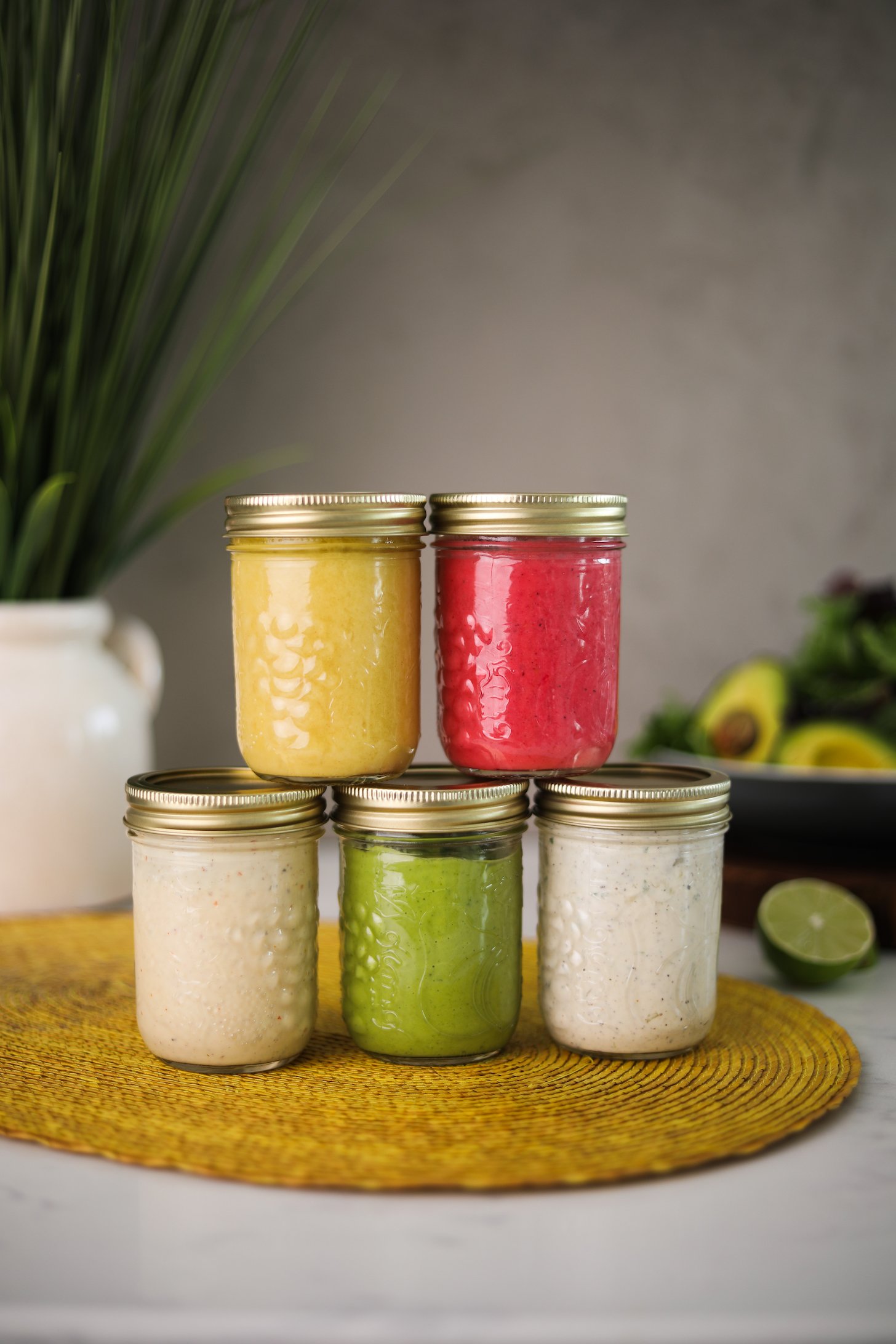 Five colourful salad dressings arranged in mason jars; three jars at the base and two jars stacked on top.