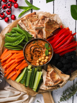 A close-up overhead image of a vibrant platter of veggies, berries, pita and hummus.
