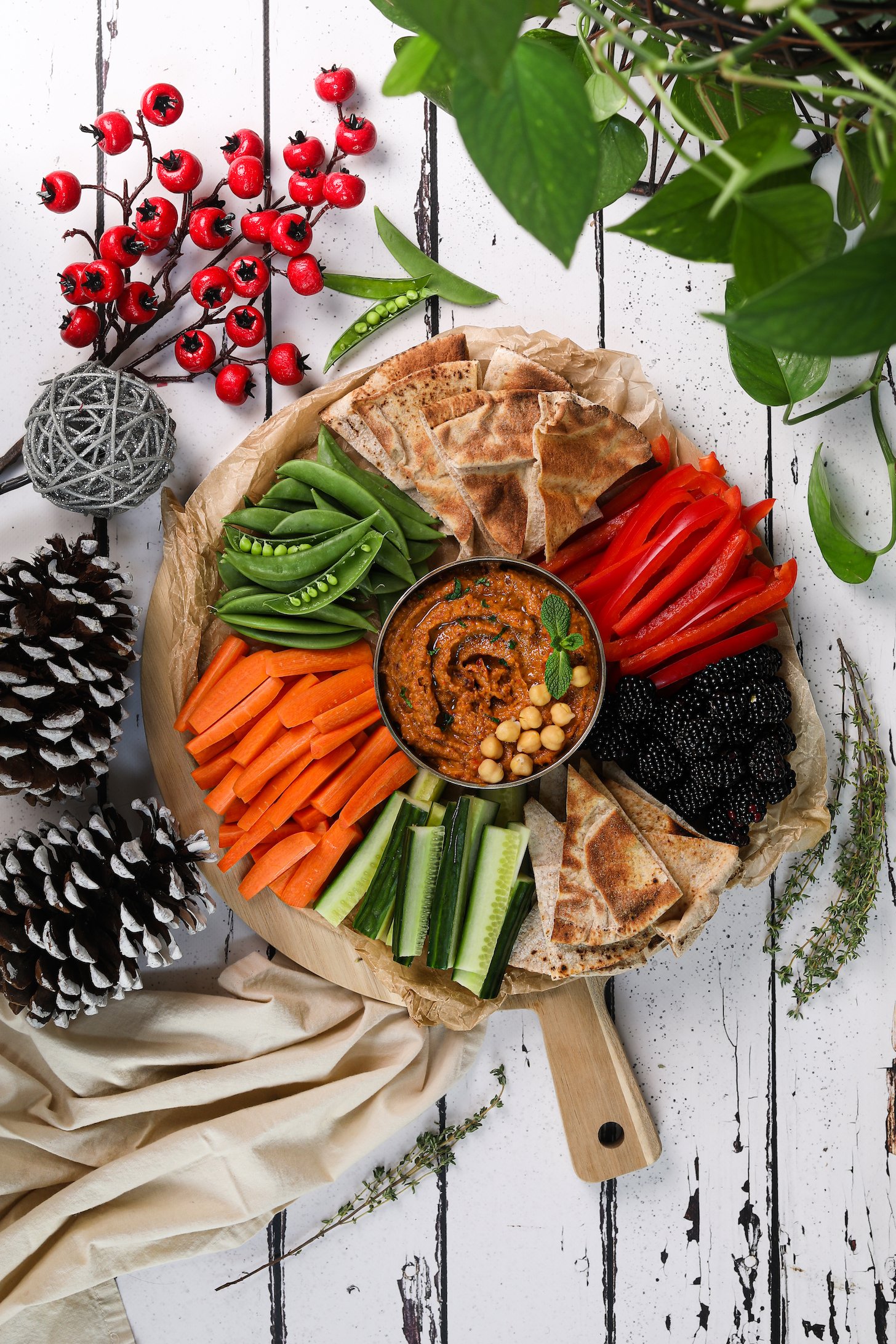 Overhead image of a vibrant platter of veggies, berries, pita and hummus styled with a holiday theme.