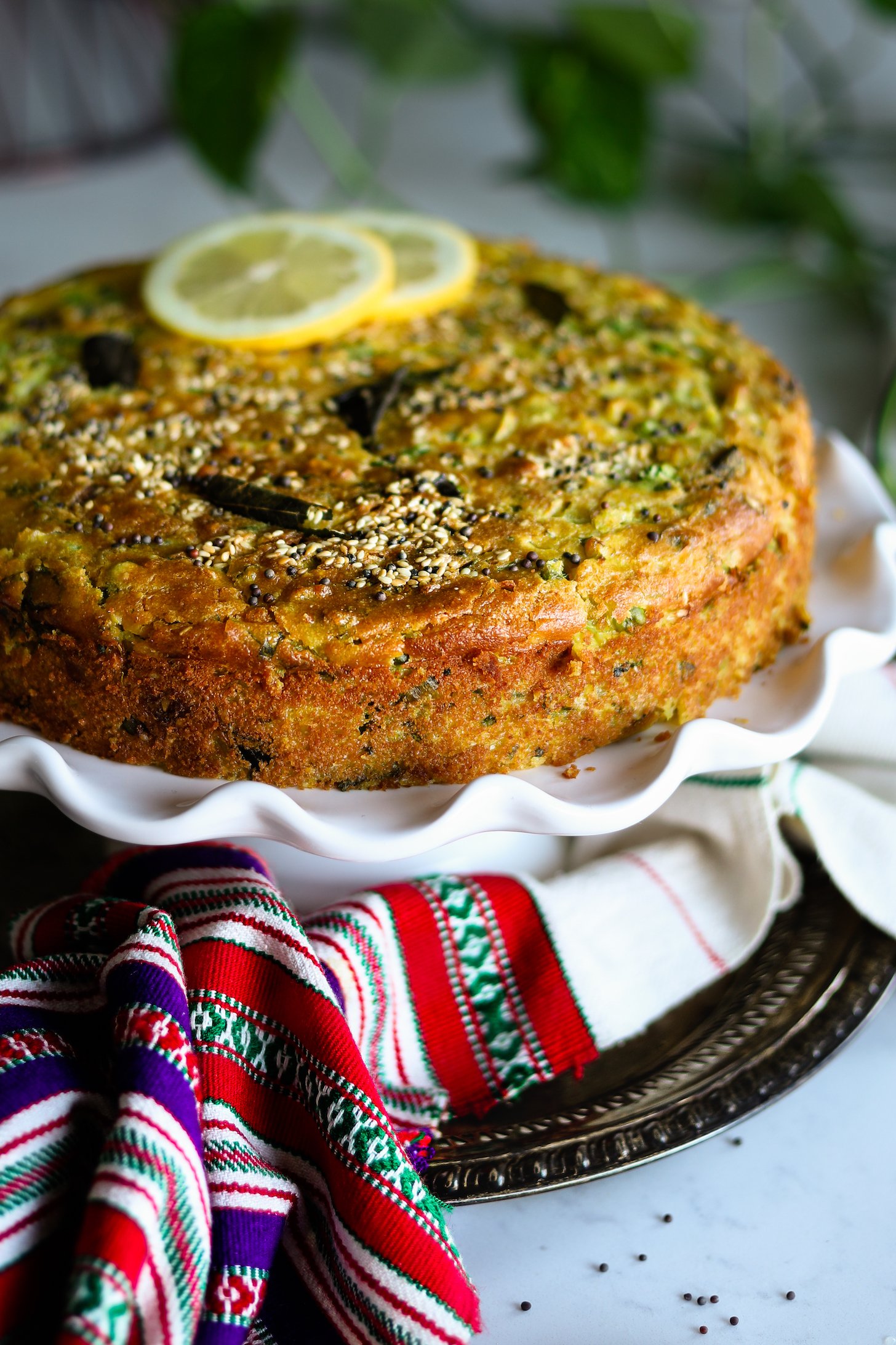 Side view of a yellow cake topped with seeds and leaves and lemon slices.