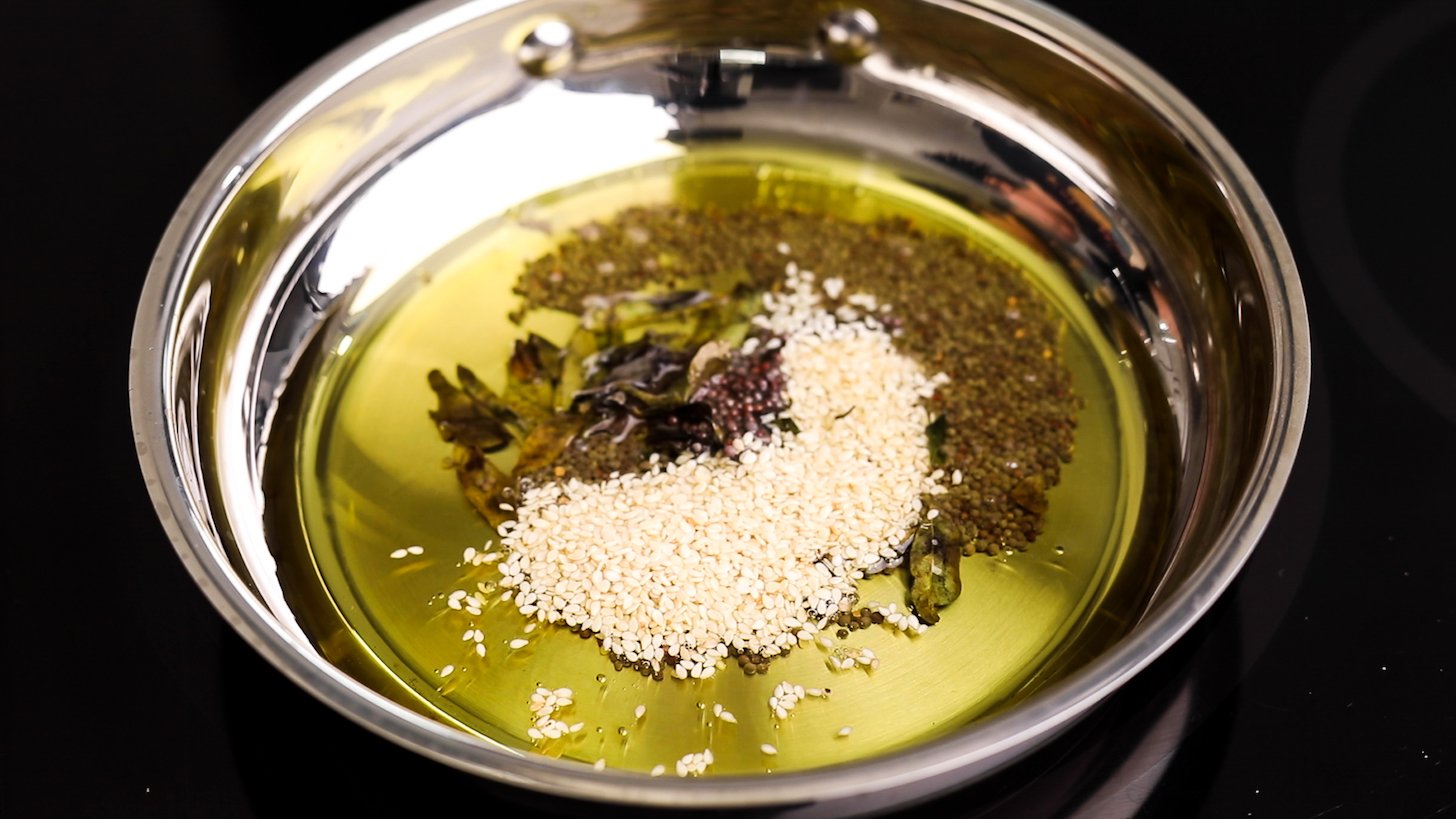 A pan of oil, seeds and curry leaves.