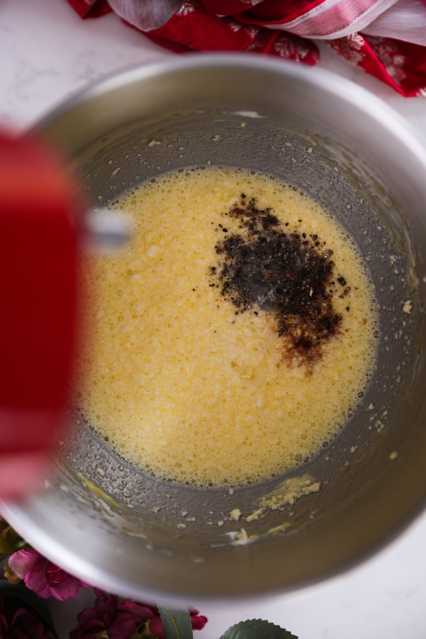 An overhead shot reveals a stand mixer bowl containing a textured, flowing yellow mixture, one area sprinkled with a dark powder.