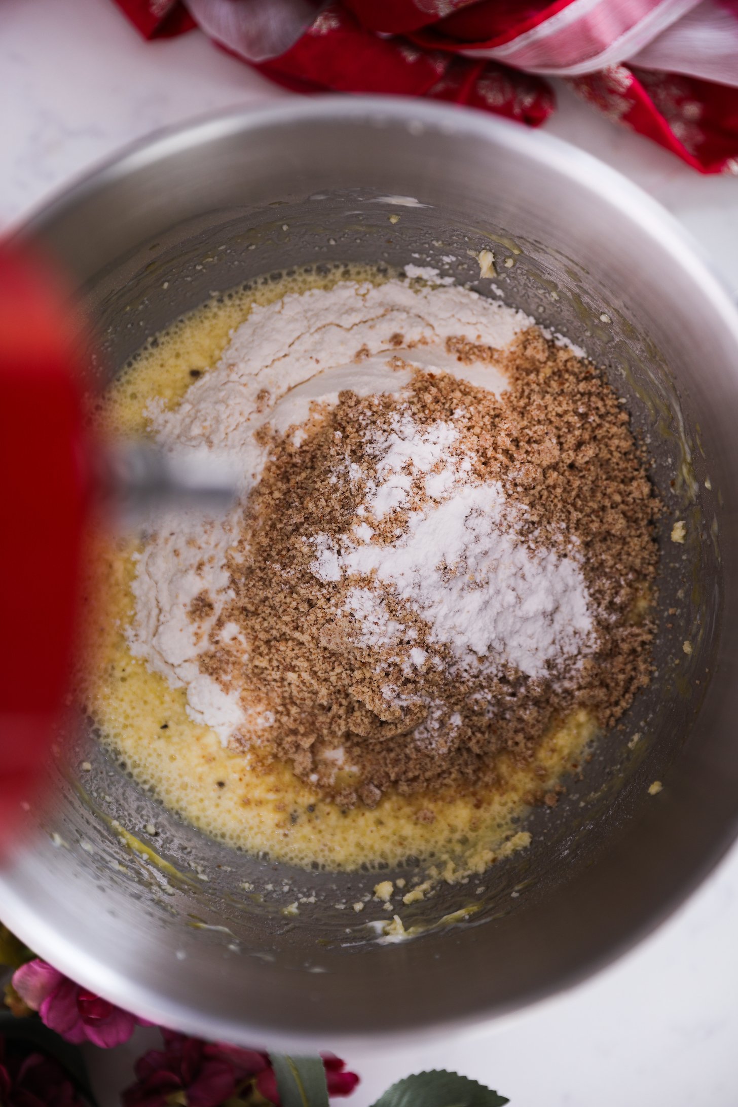 An overhead shot reveals a stand mixer bowl containing a yellow mixture topped with flour and almond meal.
