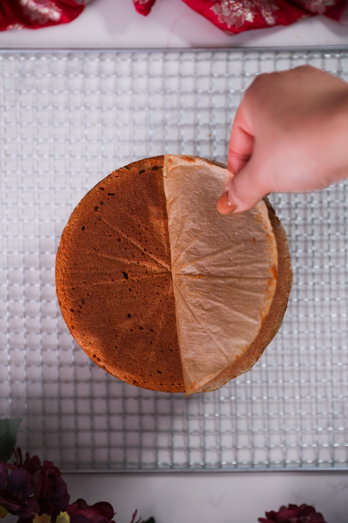 A hand peels parchment paper from a round cake positioned on a wire rack.