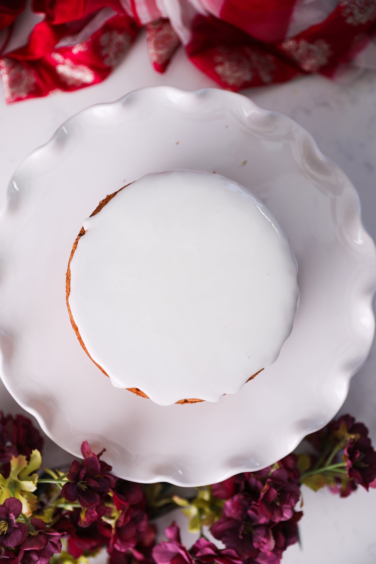 A white cake stand holds a round cake topped with smooth white icing.
