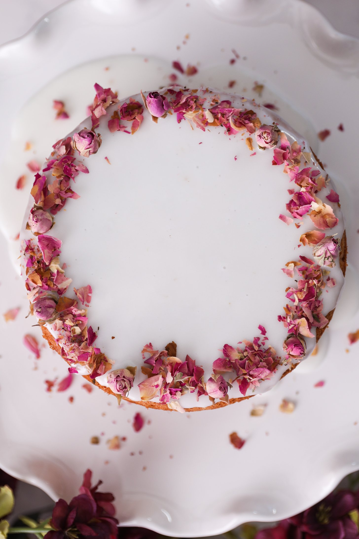 A white cake stand holds a round cake topped with smooth white icing with a boarder of red roses.