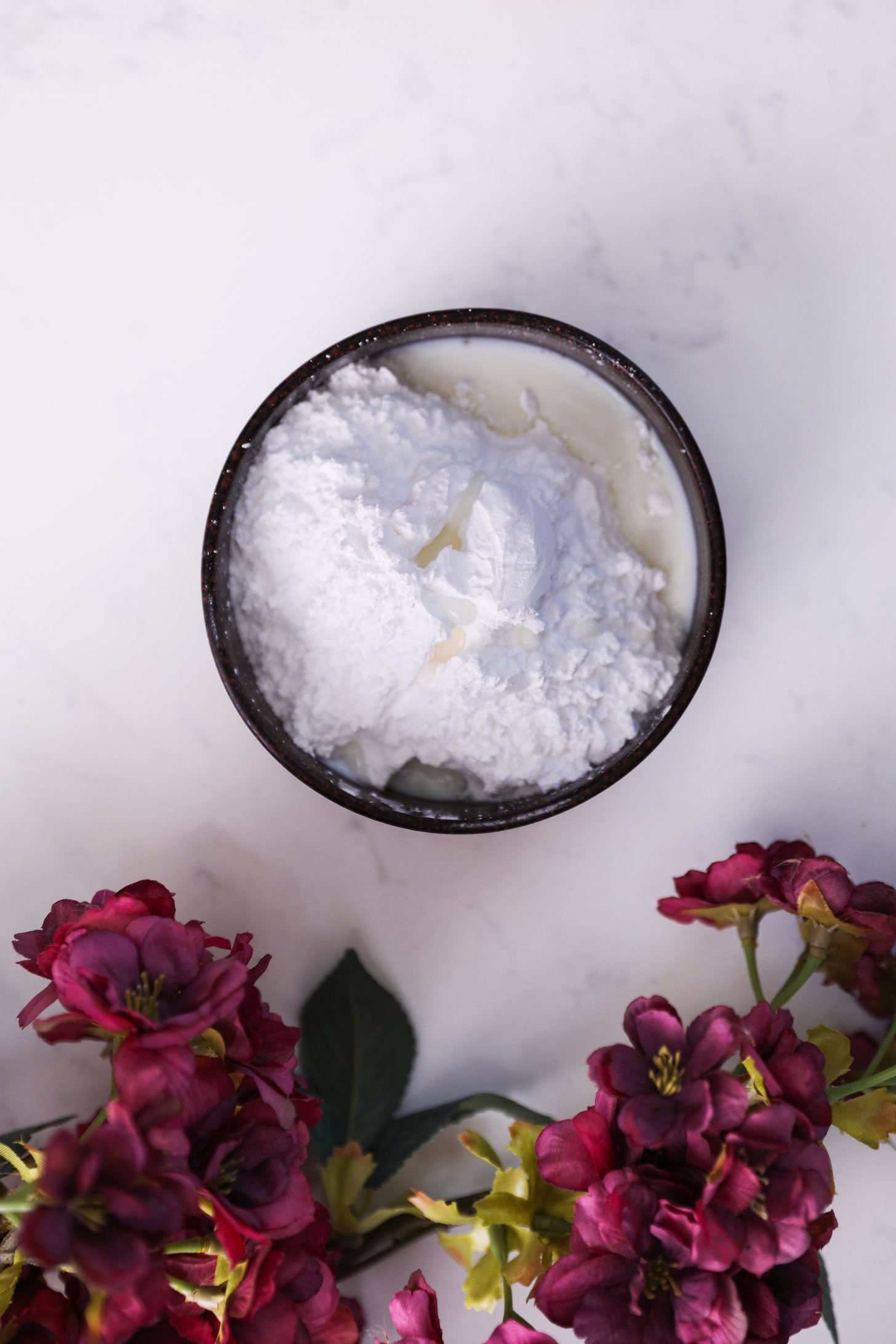 A bowl of powdered sugar with milk. There are pink flowers close by.