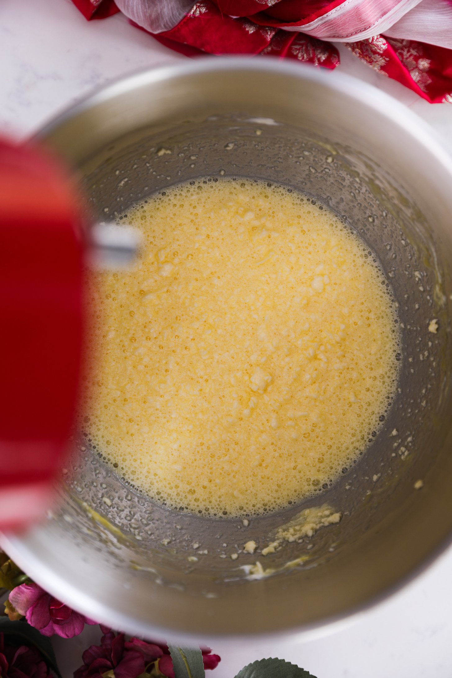 An overhead shot captures a stand mixer bowl filled with a lumpy and flowing yellow mixture.