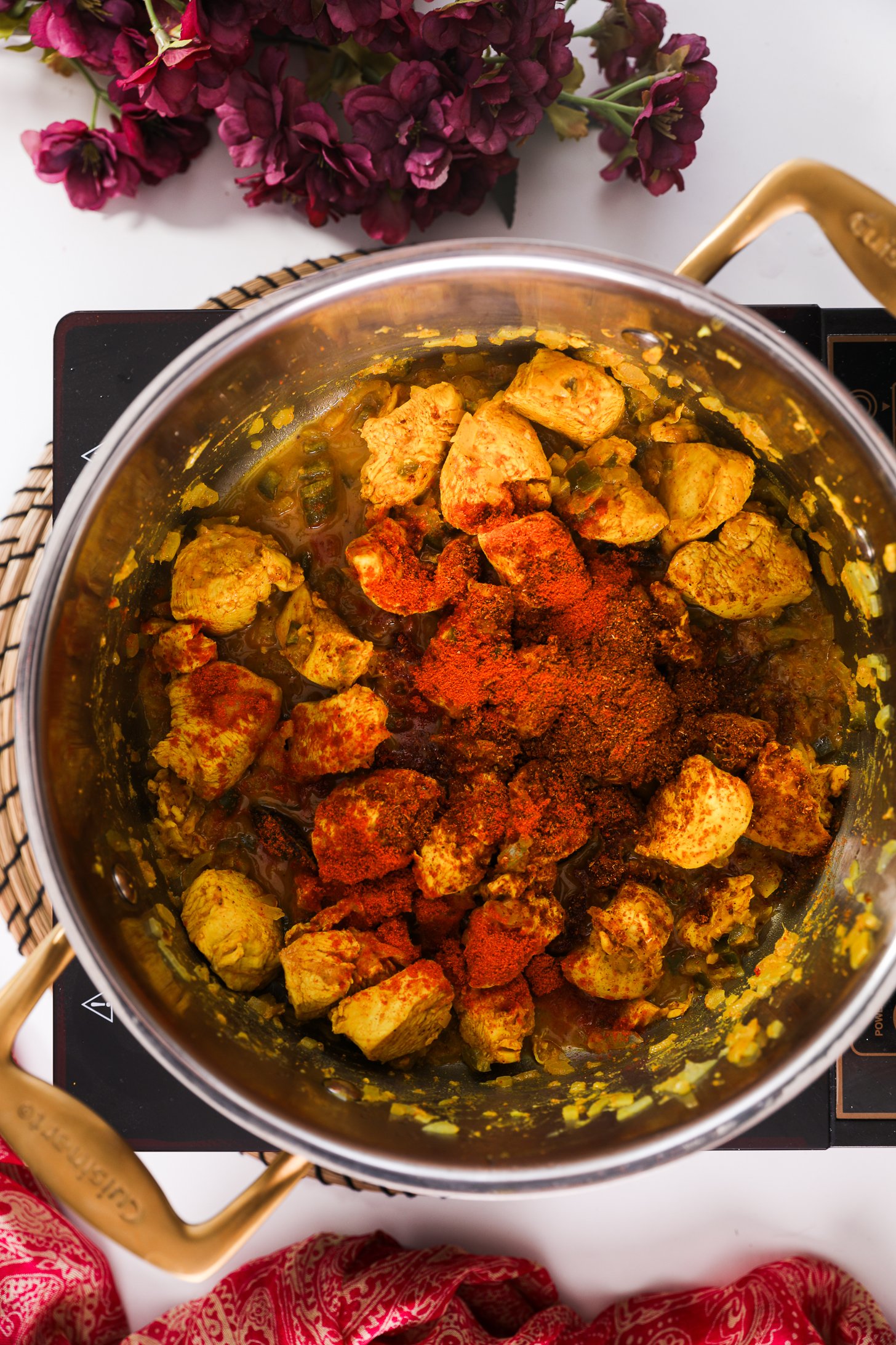 Pot on a portable surface, holding marinated cubes of chicken breast sprinkled with red spices.